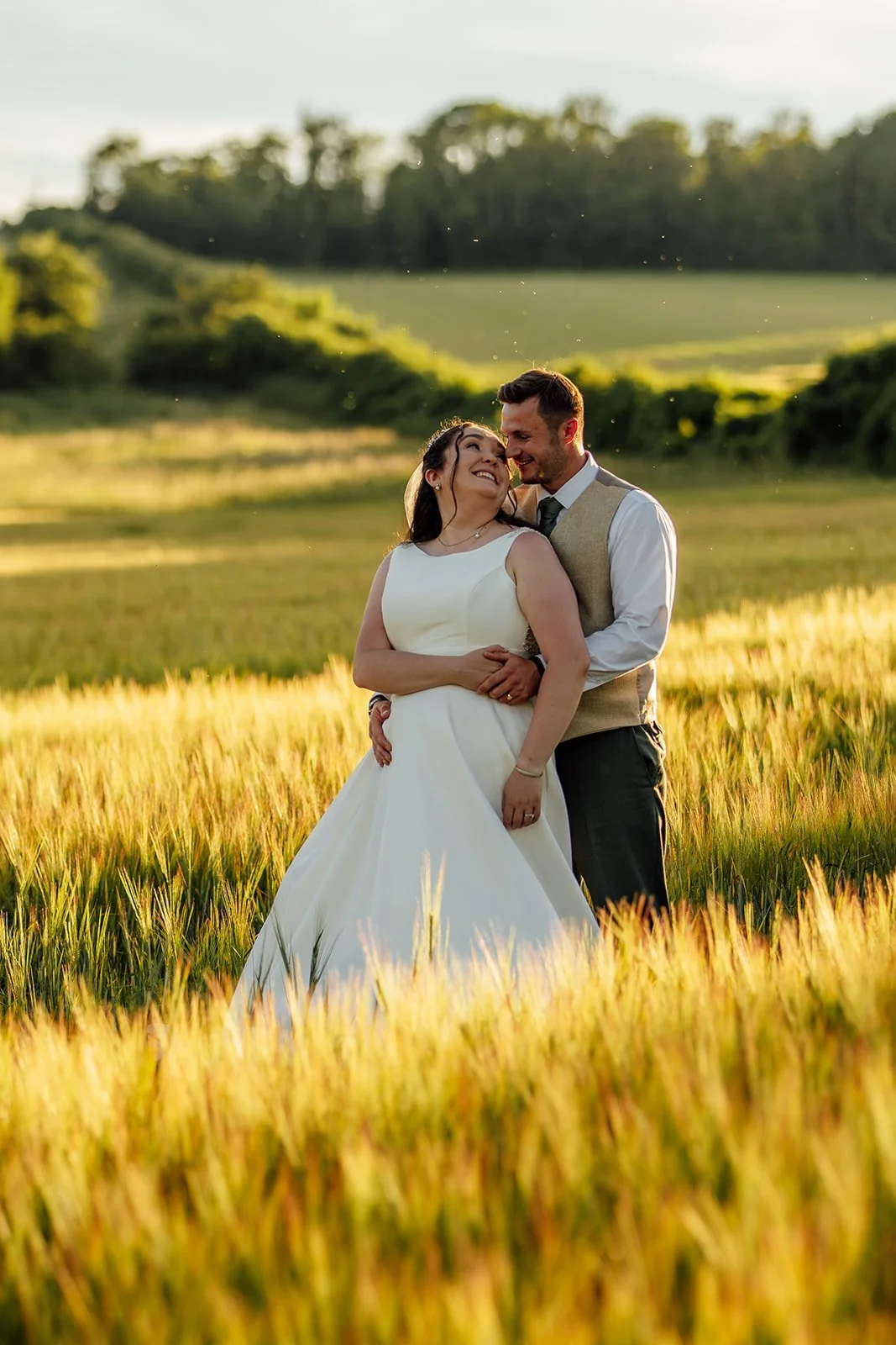 Chloe & Armani standing together in a golden field at The Barn at Upcote in the Cotswolds, photographed by Just James Weddings for warm sunset wedding portraits.