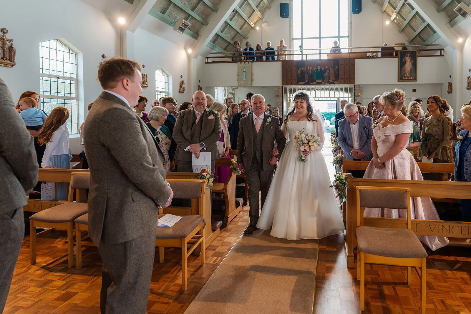 Ceremony entrance photo from Emily & Josh’s wedding at Coombe Lodge Blagdon, Somerset, UK, showing the bride walking up the aisle with family as guests look on. The church setting and emotion capture a warm, heartfelt Somerset wedding moment.