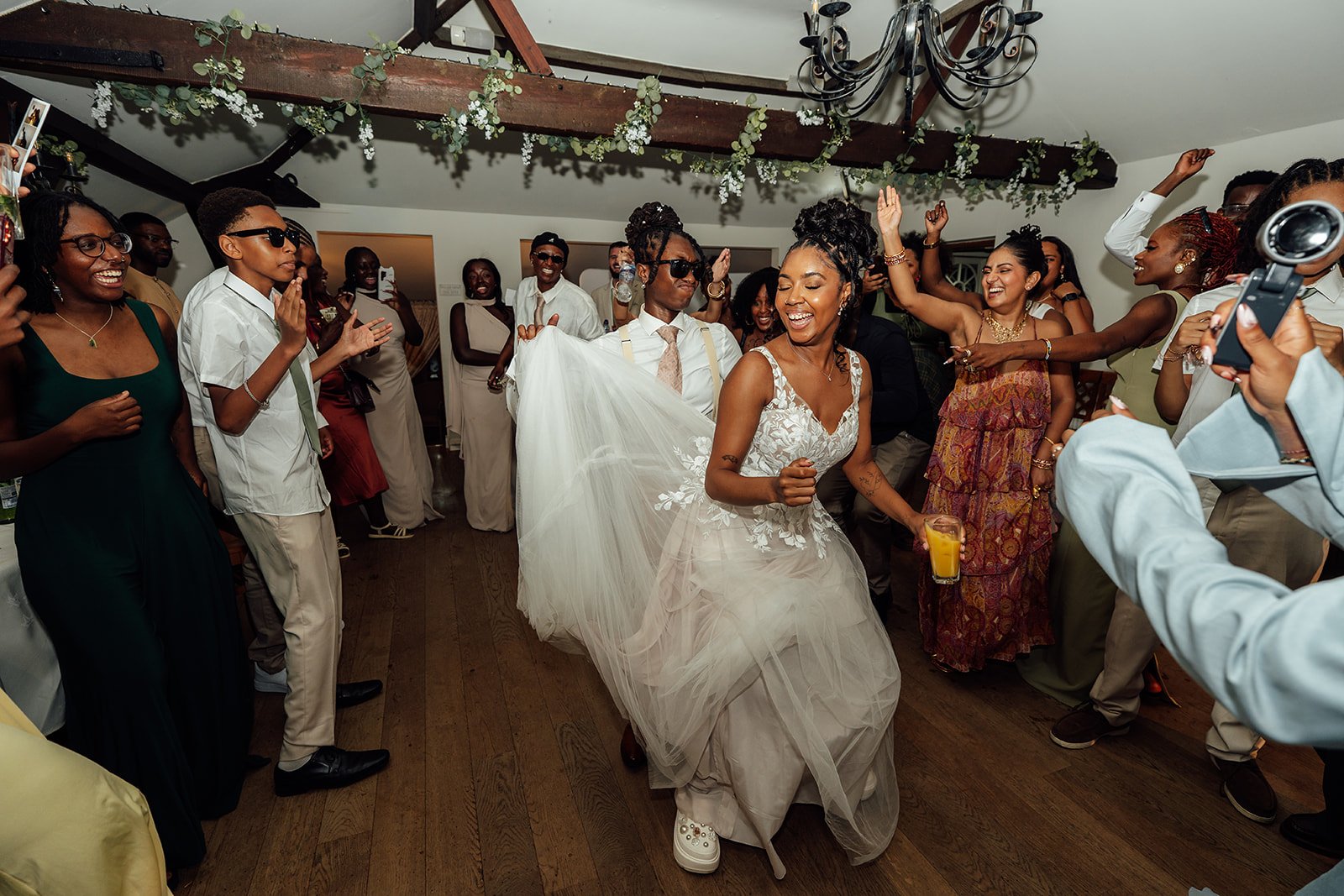 Kasey and Larisha dancing together on the packed dance floor as wedding guests cheer around them during their reception at Oaks Farm Weddings in Surrey.