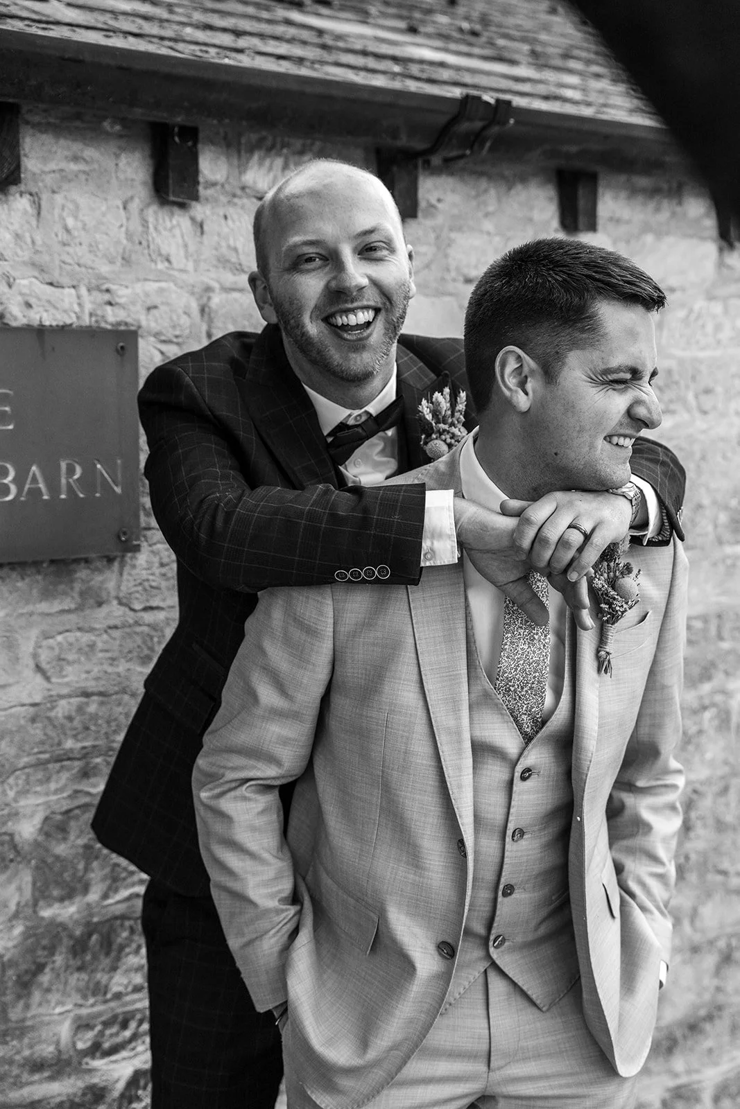 Black and white portrait of Sam & Gavin laughing together outside The Great Barn at Aynho in the Cotswolds, photographed by Just James Weddings.