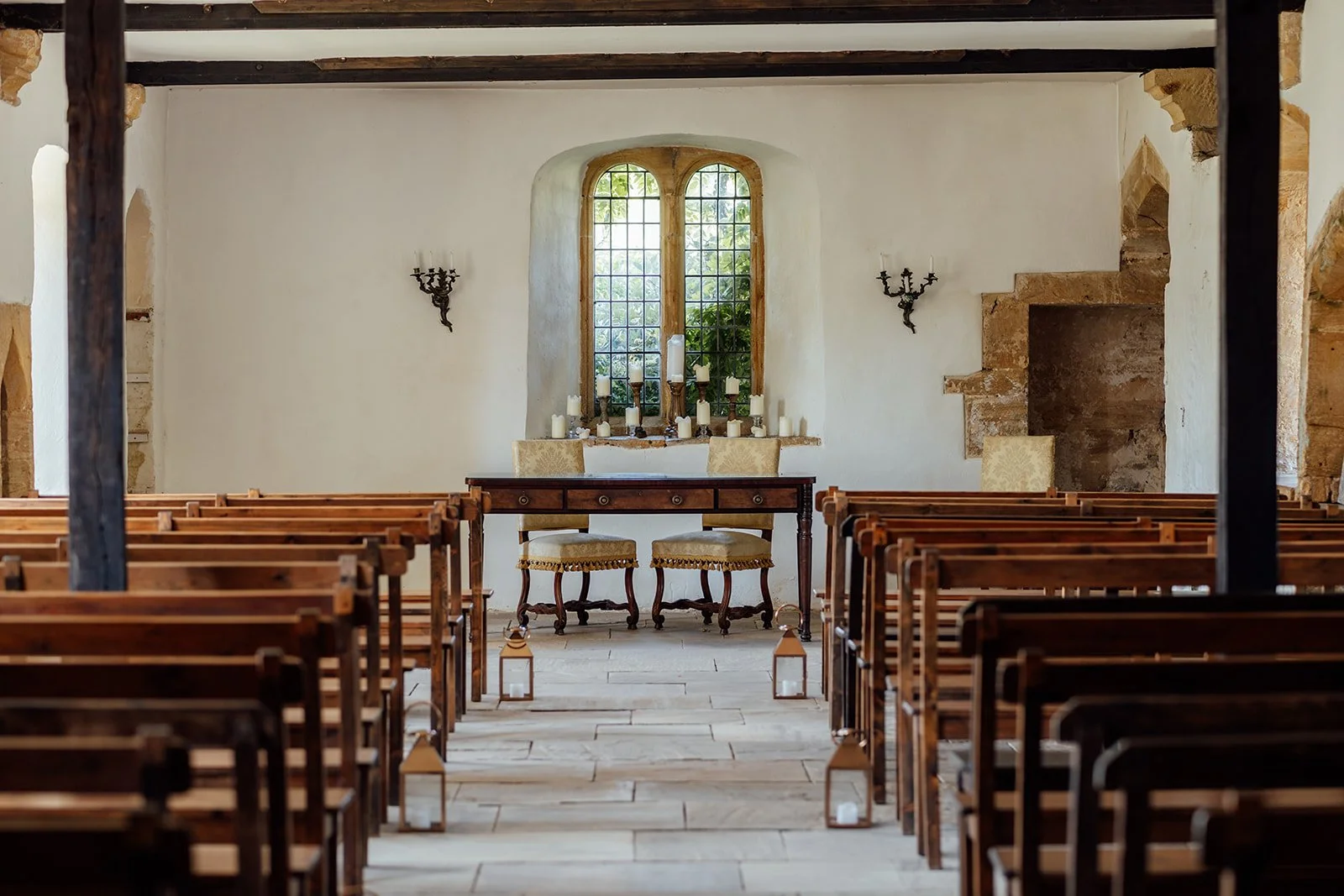Indoor ceremony space at Brympton House in Somerset, with rows of wooden benches, stone floors, candles and a historic arched window, photographed by Just James Weddings.