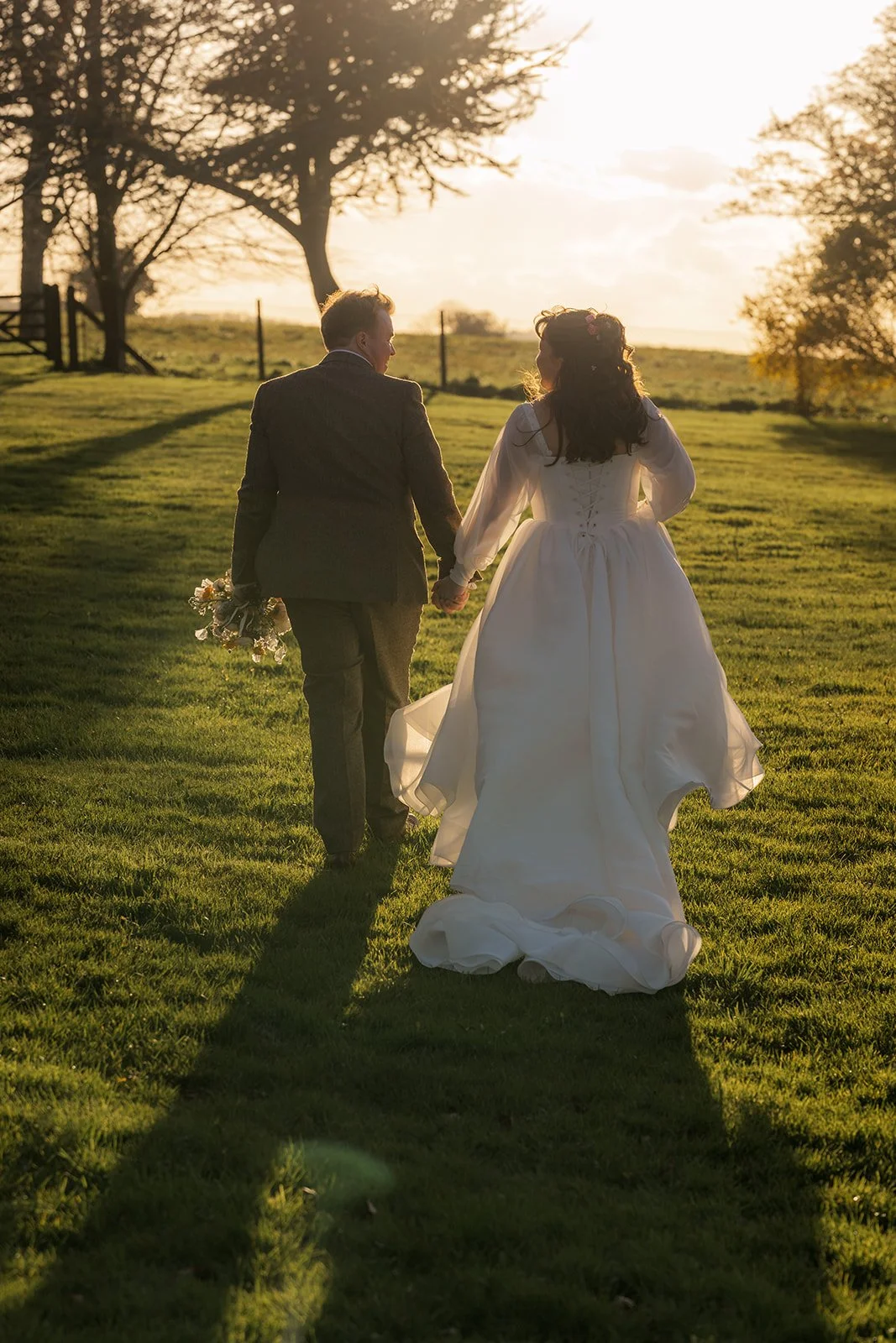 Emily and Josh walk hand in hand across the grounds of Coombe Lodge in Somerset, UK, during a golden-hour wedding portrait surrounded by warm evening light.