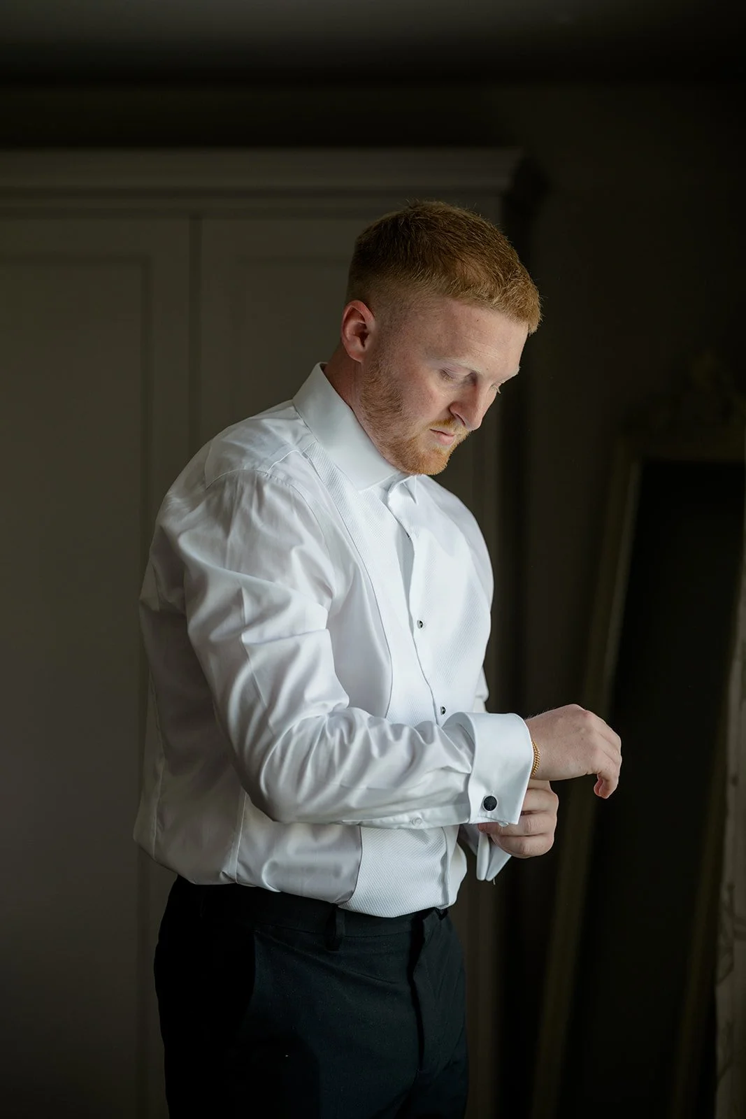 Groom prep photo of Kieran adjusting his cufflinks in a white shirt and waistcoat, lit by soft window light during Lydia & Kieran's wedding morning at Hencote Estate in Shropshire, UK, before the ceremony and celebrations begin indoors quietly.