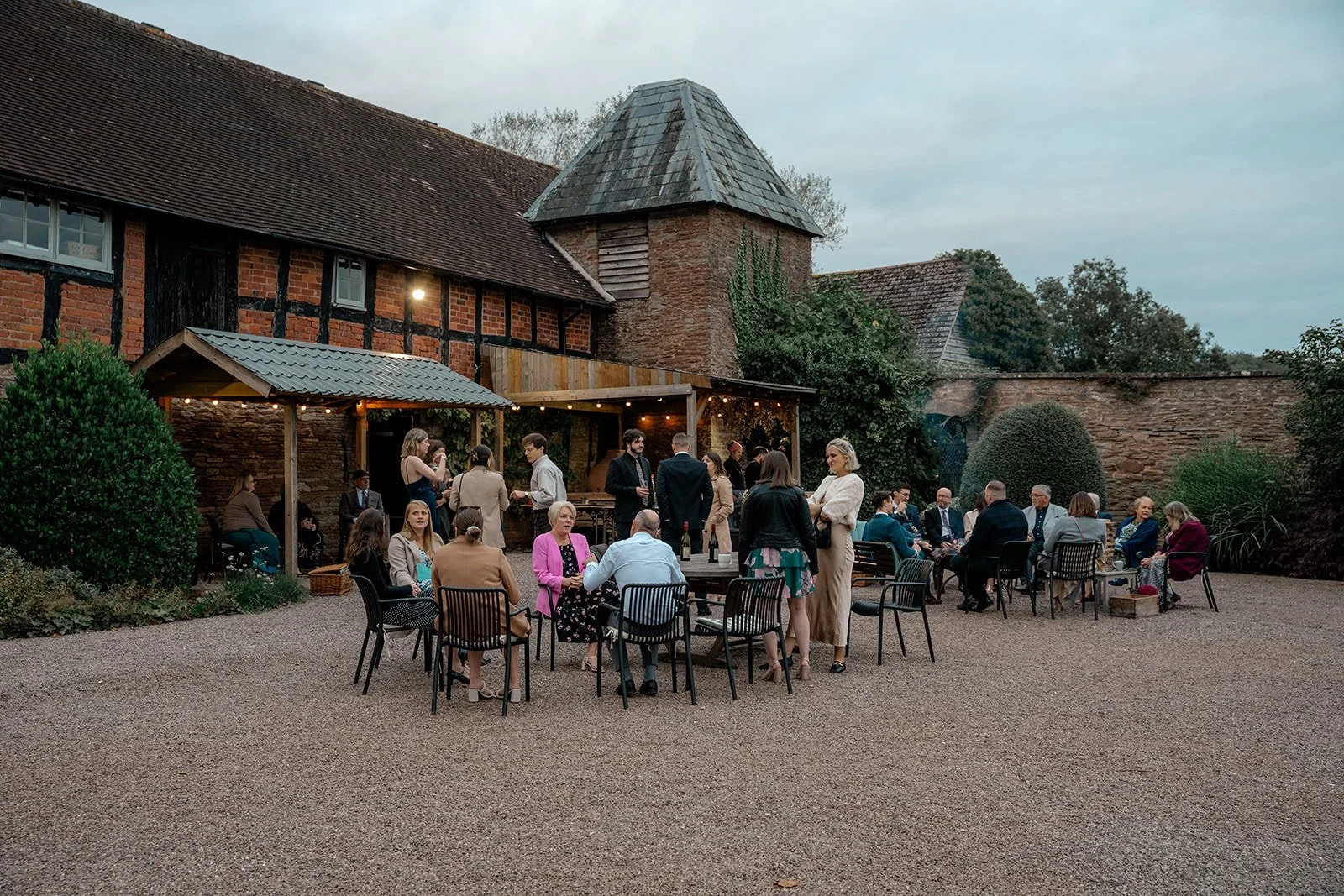 Wedding guests dining outside in the courtyard at Broadfield Court in Herefordshire, surrounded by historic timber buildings, photographed by Just James Weddings for reception atmosphere.