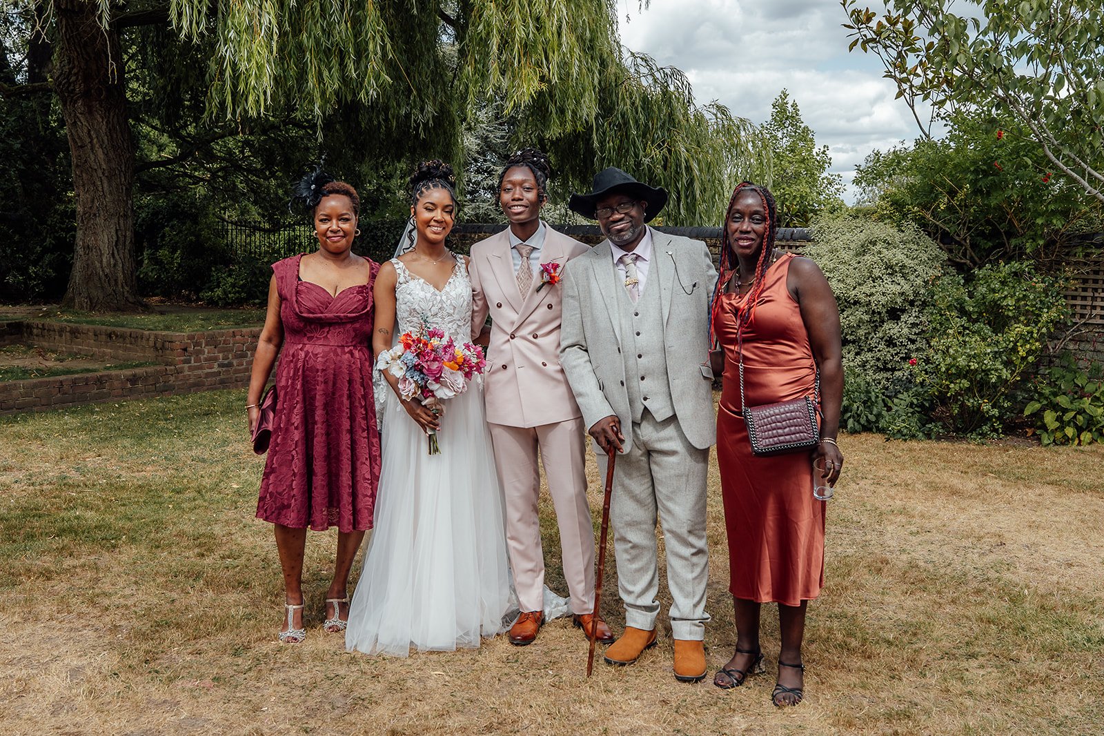 Kasey and Larisha posing with family members for a relaxed group portrait in the gardens at Oaks Farm Weddings in Surrey.