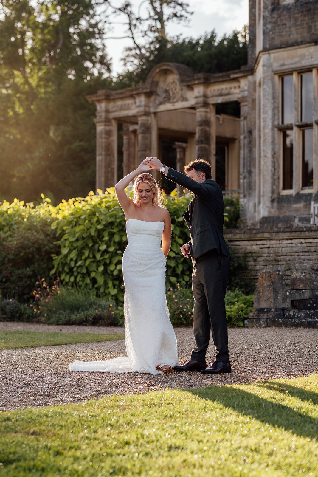 Amy & Matt dance together in golden evening light outside Orchardleigh Estate in Somerset, with the historic manor house and gardens behind them, captured by Just James Weddings.