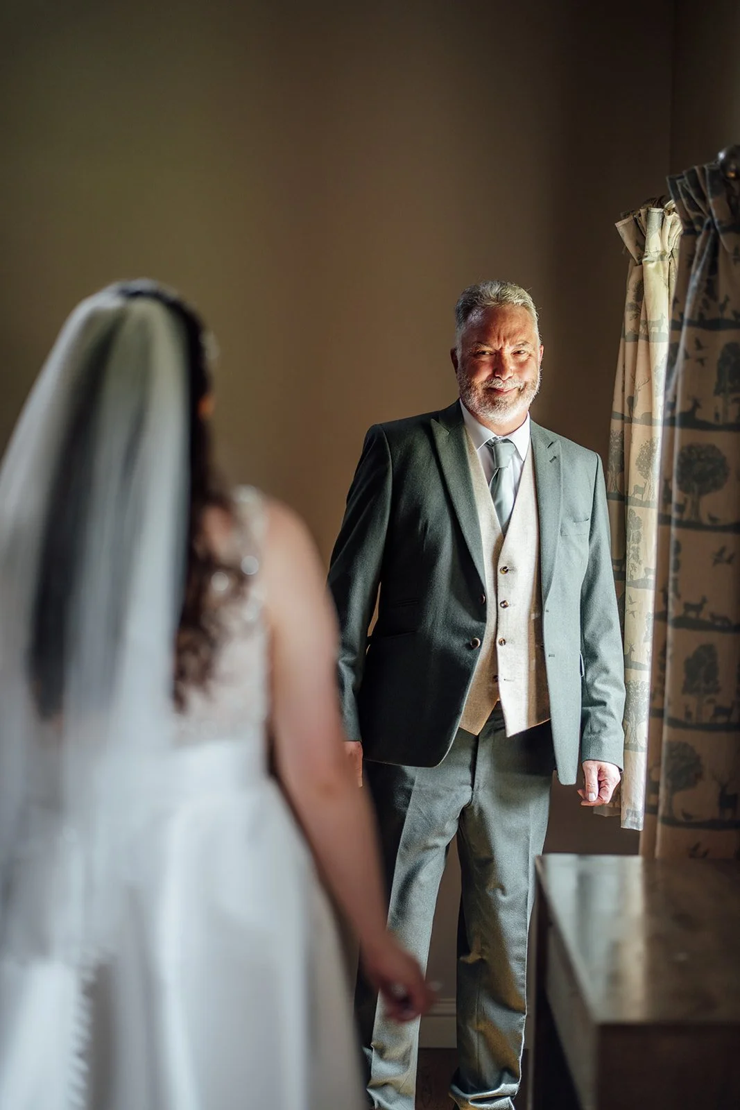 Chloe’s father smiles as he sees her in her wedding dress before she marries Armani at The Barn at Upcote in Gloucestershire, photographed by Just James Weddings.