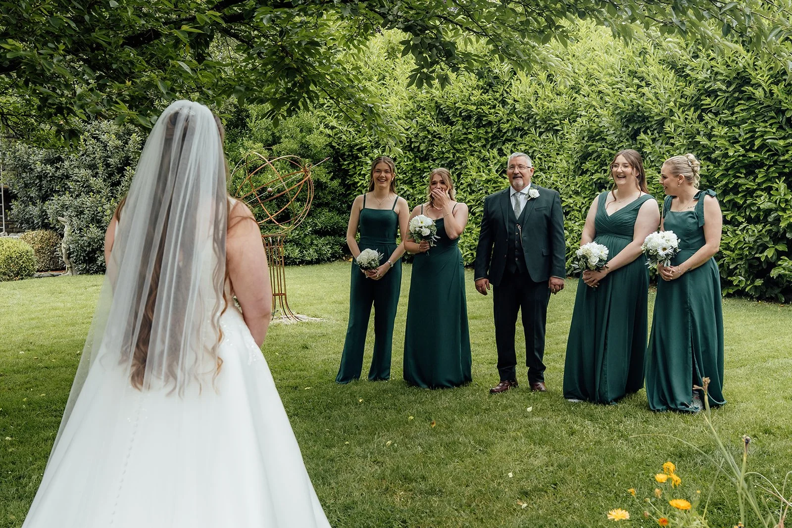 Emotional first look with bridesmaids and family in the garden for Louise & Jon’s wedding at Wick Farm Bath in Somerset, UK, with green dresses, white bouquets, lush summer foliage, laughter, and a joyful bridal reveal moment.