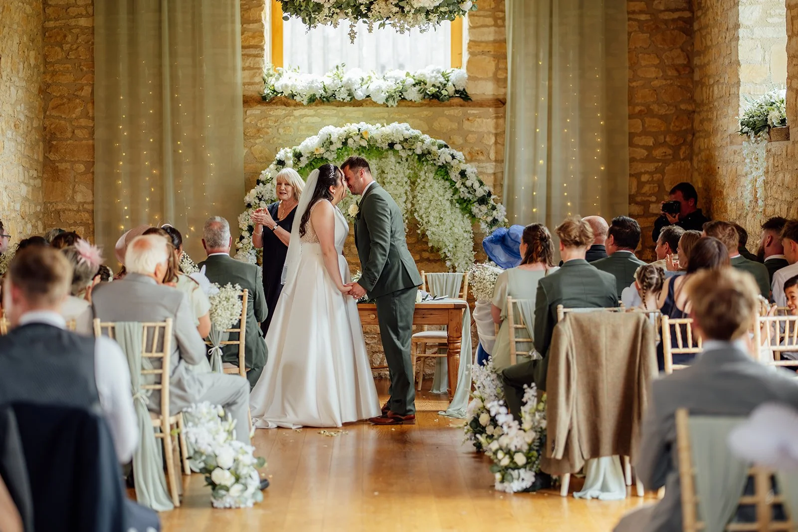 Chloe & Armani sharing their first kiss during their indoor ceremony at The Barn at Upcote in the Cotswolds, photographed by Just James Weddings.