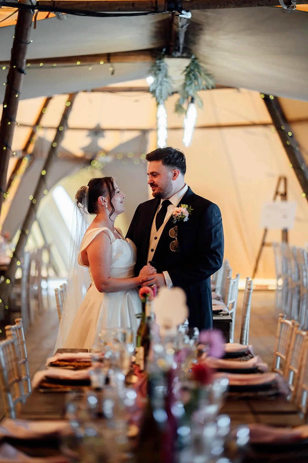 Harriet & Simon share a quiet moment beside the reception tables inside the tipi at Dovecote Events in Oxfordshire, photographed by Just James Weddings.