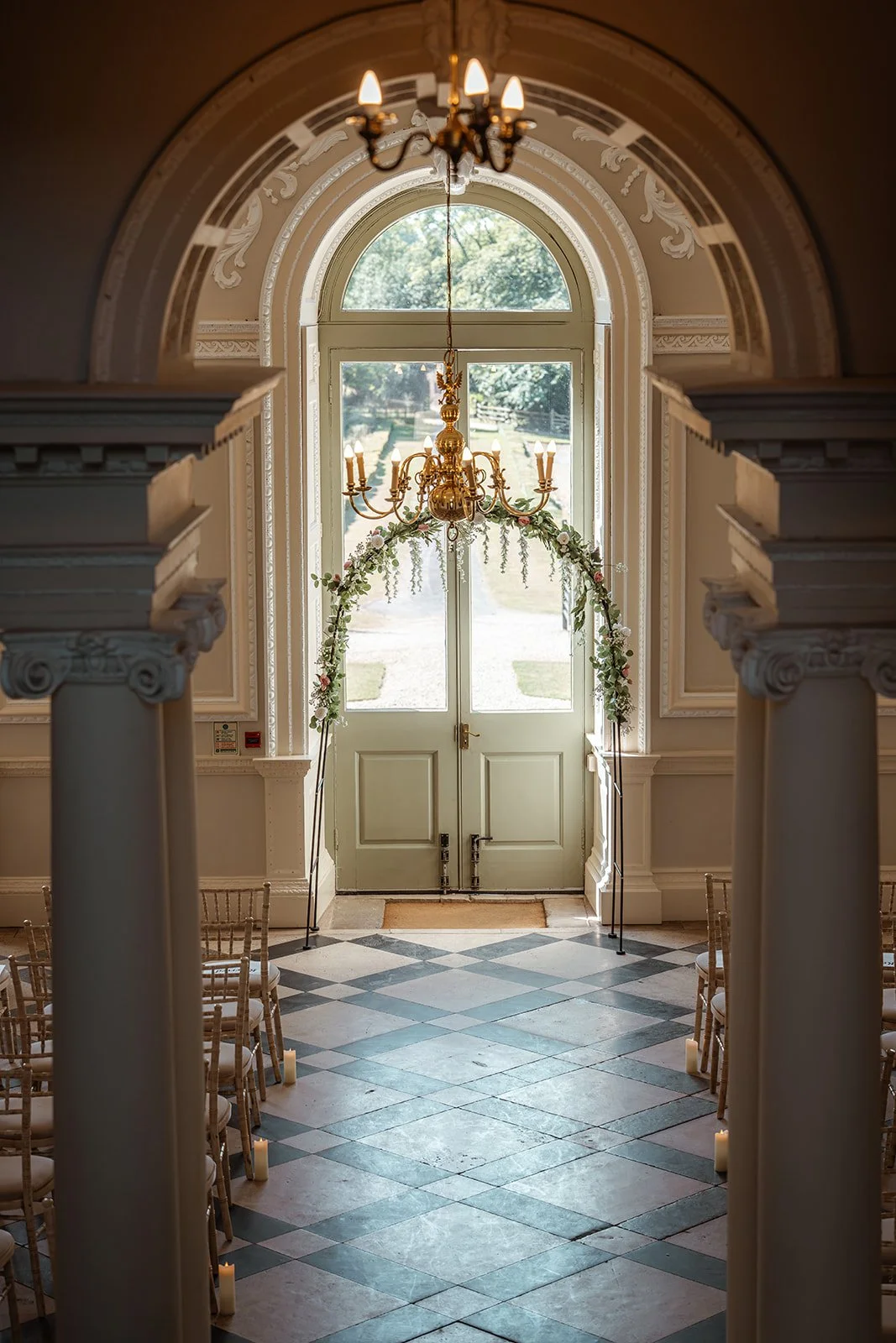 Indoor ceremony room at Crowcombe Court in the UK, with classic columns, arched doorway, chairs and floral styling, photographed by Just James Weddings for elegant venue inspiration.