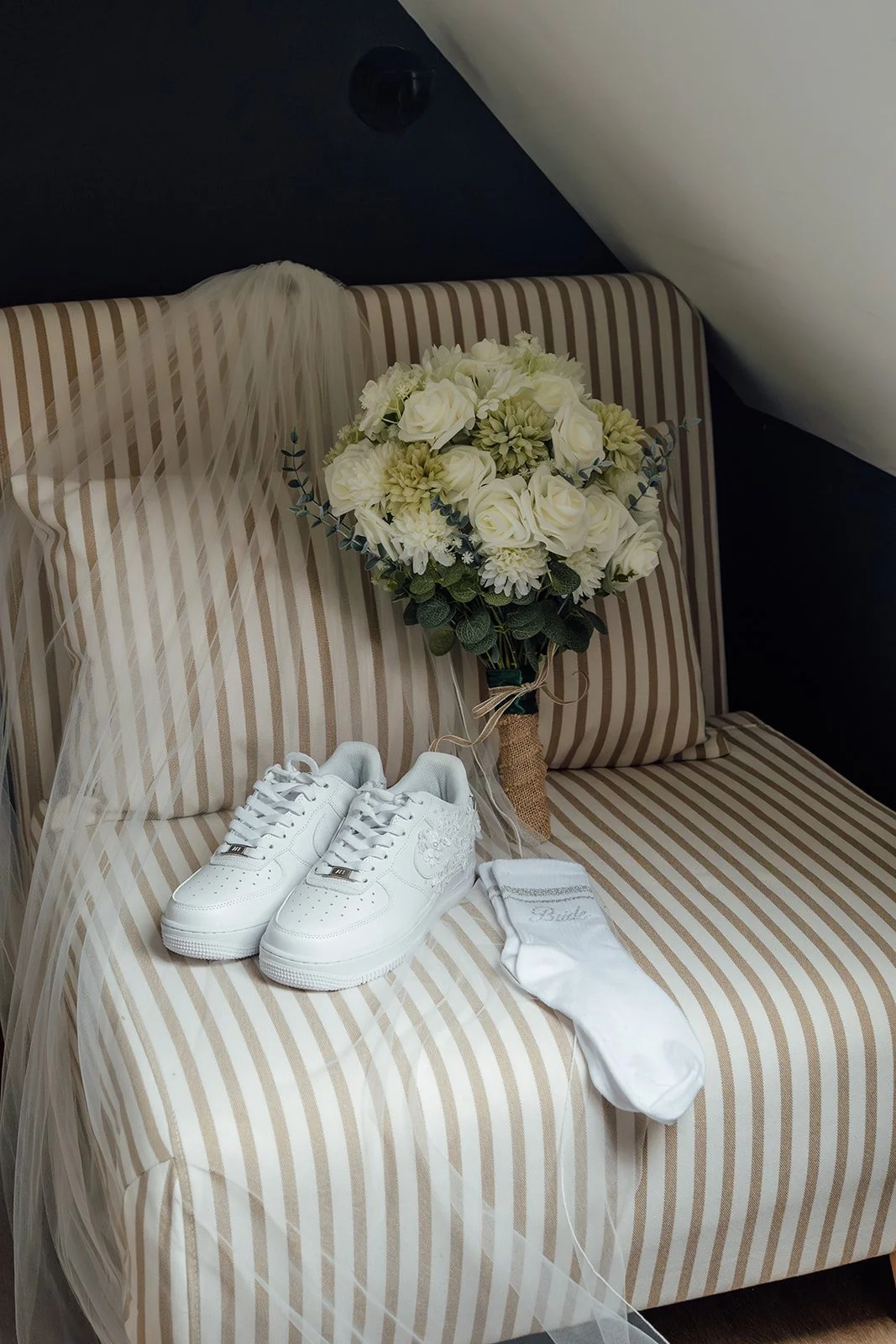 Wedding bouquet, veil, bridal trainers and personalised socks styled on a striped chair for Louise & Jon’s wedding at Wick Farm Bath in Somerset, UK, capturing elegant bridal details with soft cream flowers and relaxed modern styling.