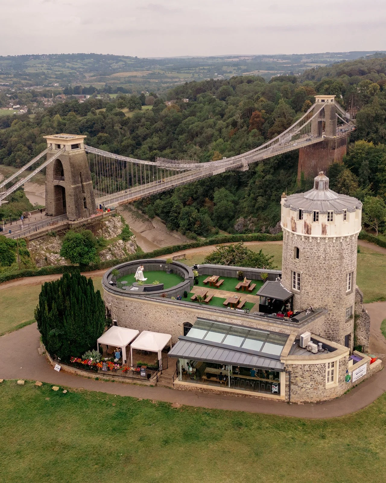 Drone view of Clifton Observatory in Somerset, with the Clifton Suspension Bridge and terrace beside the tower, photographed by Just James Weddings for unique wedding venue imagery.