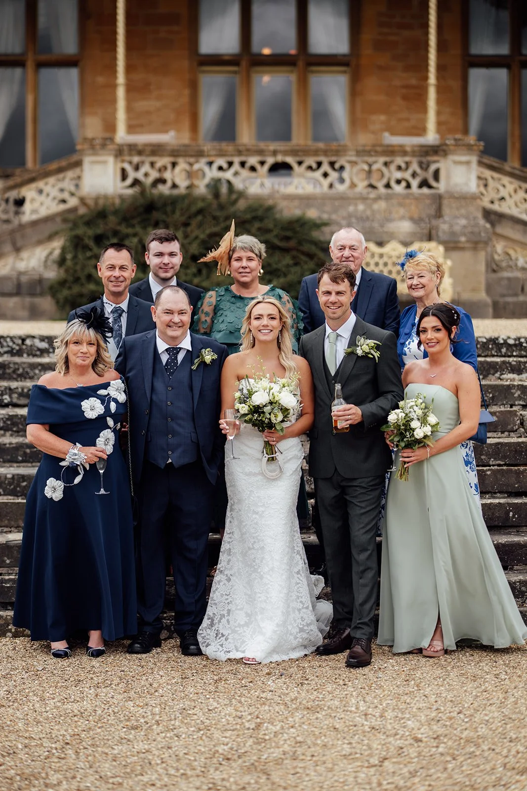 Formal family portrait of Amy & Matt with relatives and wedding party on the stone steps outside Orchardleigh Estate in Somerset, captured after the ceremony by Just James Weddings.