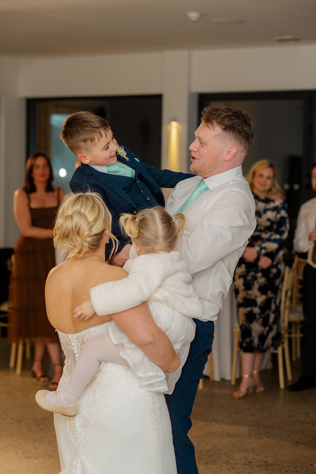 Andrew lifting his young son on the dance floor at Andrew & Daisy’s Sandy Cove Hotel wedding in Devon, while Daisy holds their daughter nearby, capturing joyful family moments during the evening reception at this coastal wedding venue.