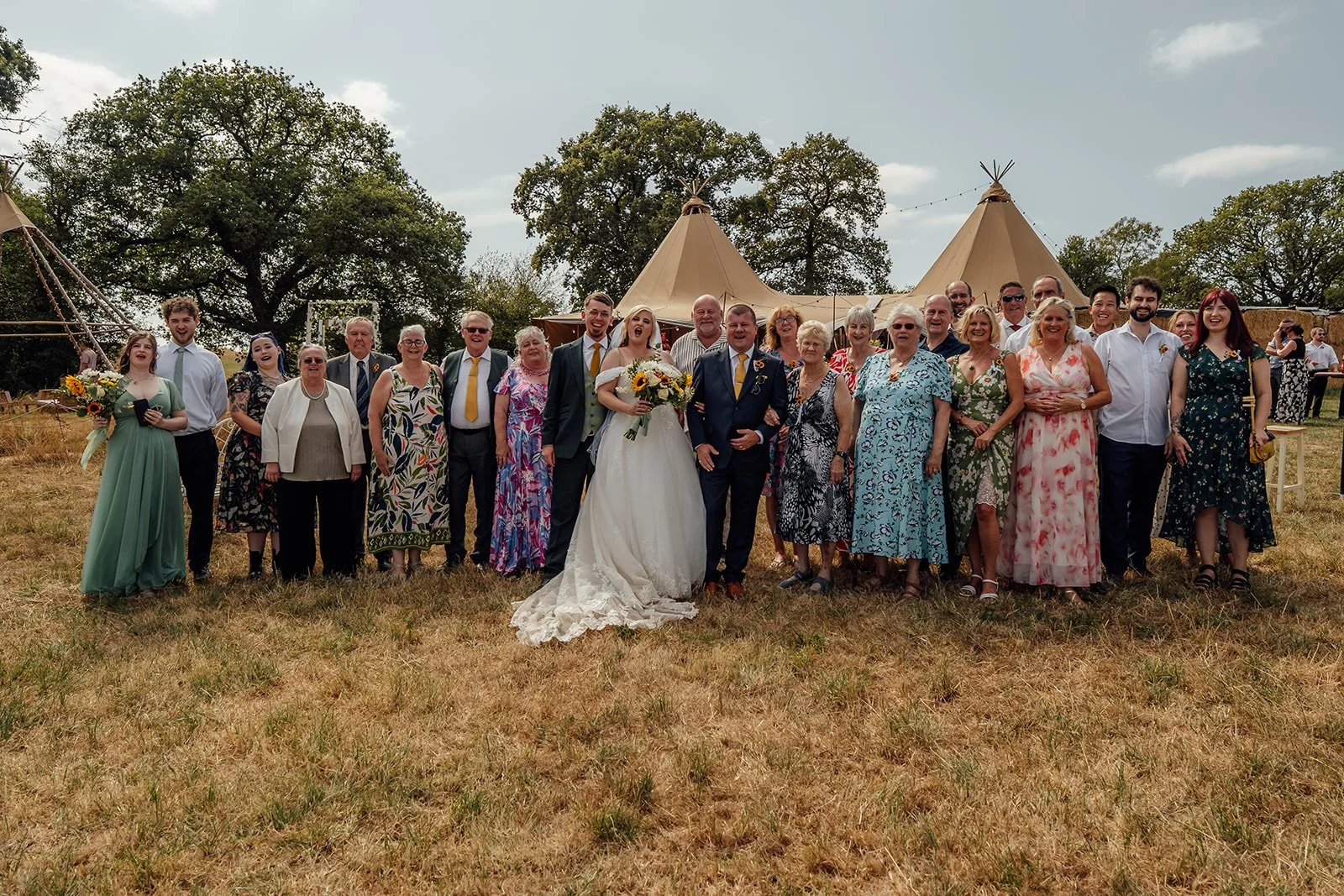 Lucy and Matthew standing with family and wedding guests for a large outdoor group photo at Curated Canvas at Noah’s Pond in Somerset, photographed by Just James Weddings.