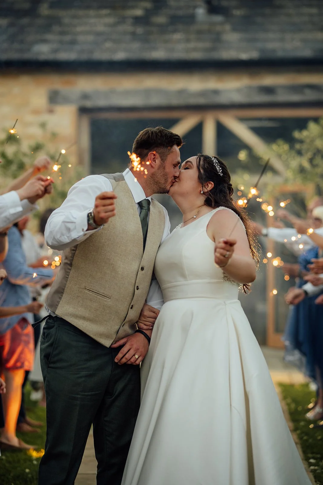 Chloe and Armani kiss while walking through a sparkler send-off outside The Barn at Upcote in Gloucestershire, photographed by Just James Weddings.