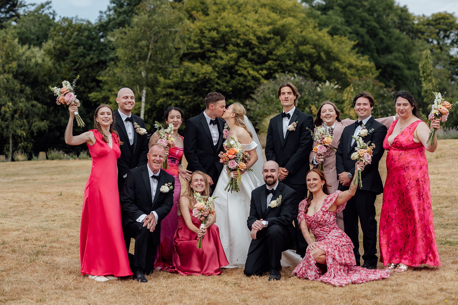 Caitlin and Kevin kissing during a fun wedding party group photo at Clevedon Hall in Somerset, surrounded by bridesmaids and groomsmen holding colourful bouquets.