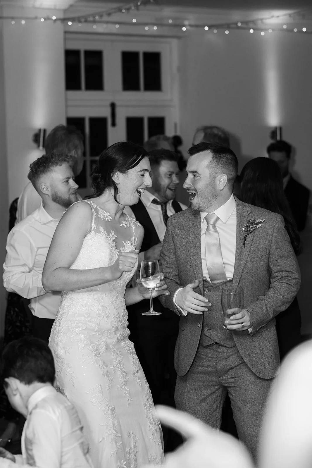 Anna and Chris dance together at their Elmhay Park wedding in Somerset, UK, laughing with drinks in hand as guests celebrate around them. A lively black and white reception moment from Anna & Chris’s wedding day, full of joy, energy, and fun.