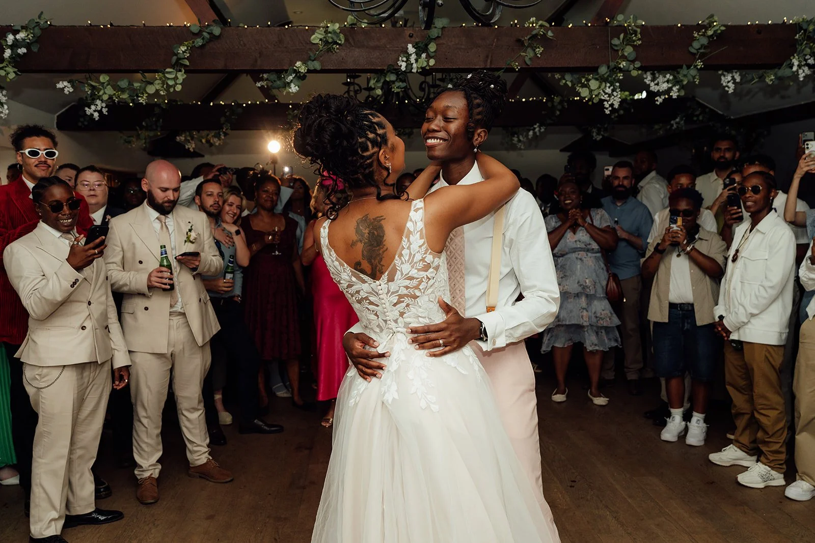 Kasey and Larisha smiling together during their first dance as wedding guests gather around them at Oaks Farm Weddings in Surrey.