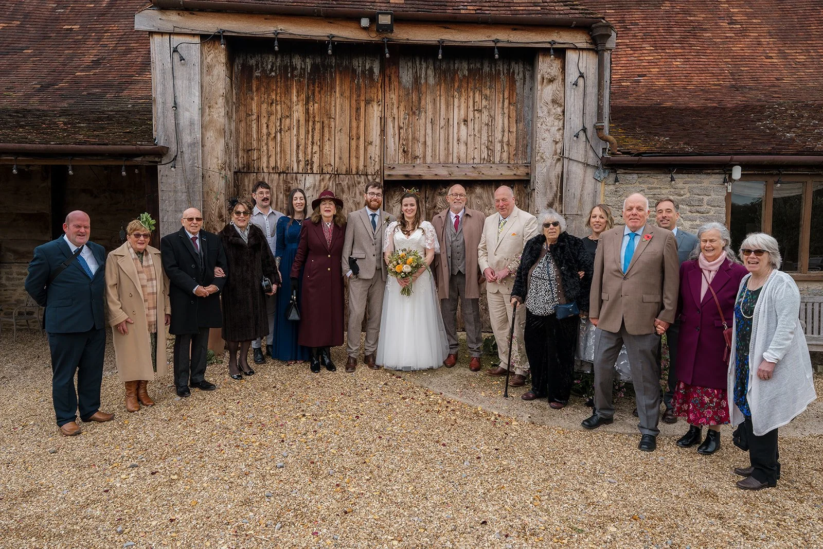 Maisie & Andrew standing with family and wedding guests outside the rustic barn at Stockbridge Farm Barn in Dorset, photographed by Just James Weddings.