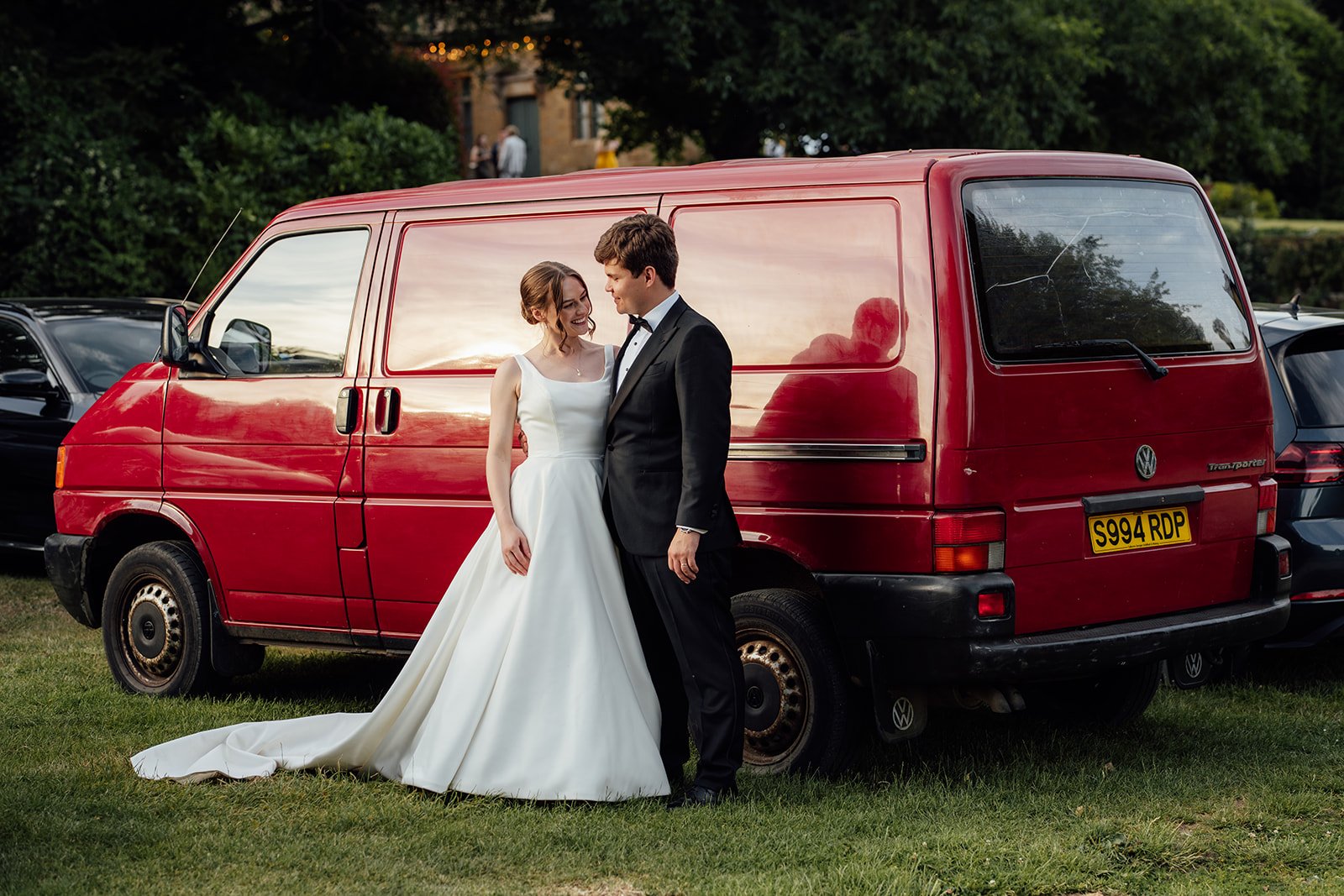 Rachel & Tom pose beside a red Volkswagen van on the grounds of Brympton House in Somerset, photographed by Just James Weddings.