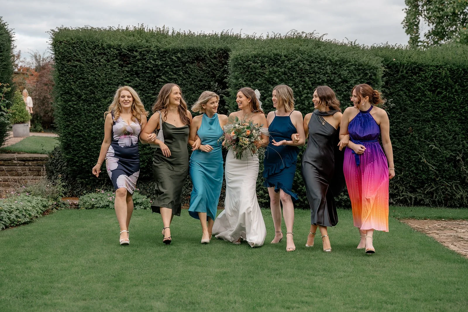 Lilly walking through the gardens with her bridesmaids at Broadfield Court in Herefordshire, photographed by Just James Weddings for relaxed and colourful wedding party portraits.