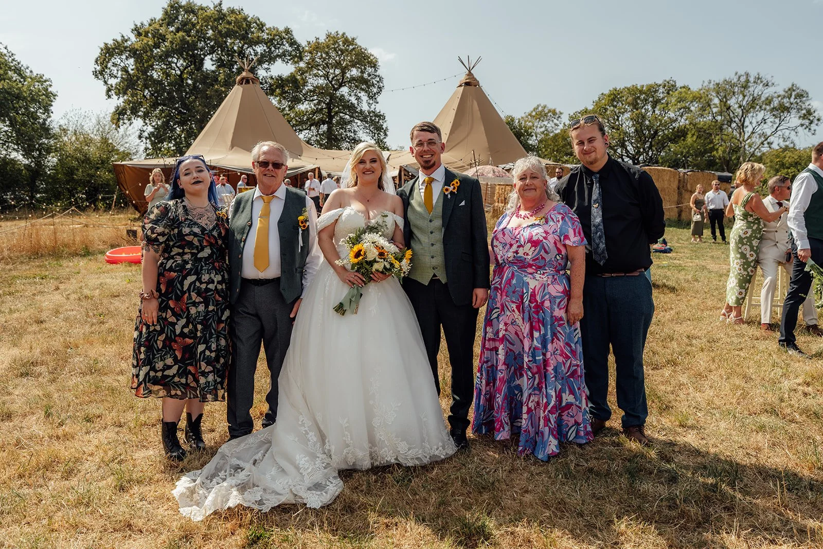 Lucy and Matthew posing with close family members in front of the tipi wedding reception at Curated Canvas at Noah’s Pond in Somerset, photographed by Just James Weddings.
