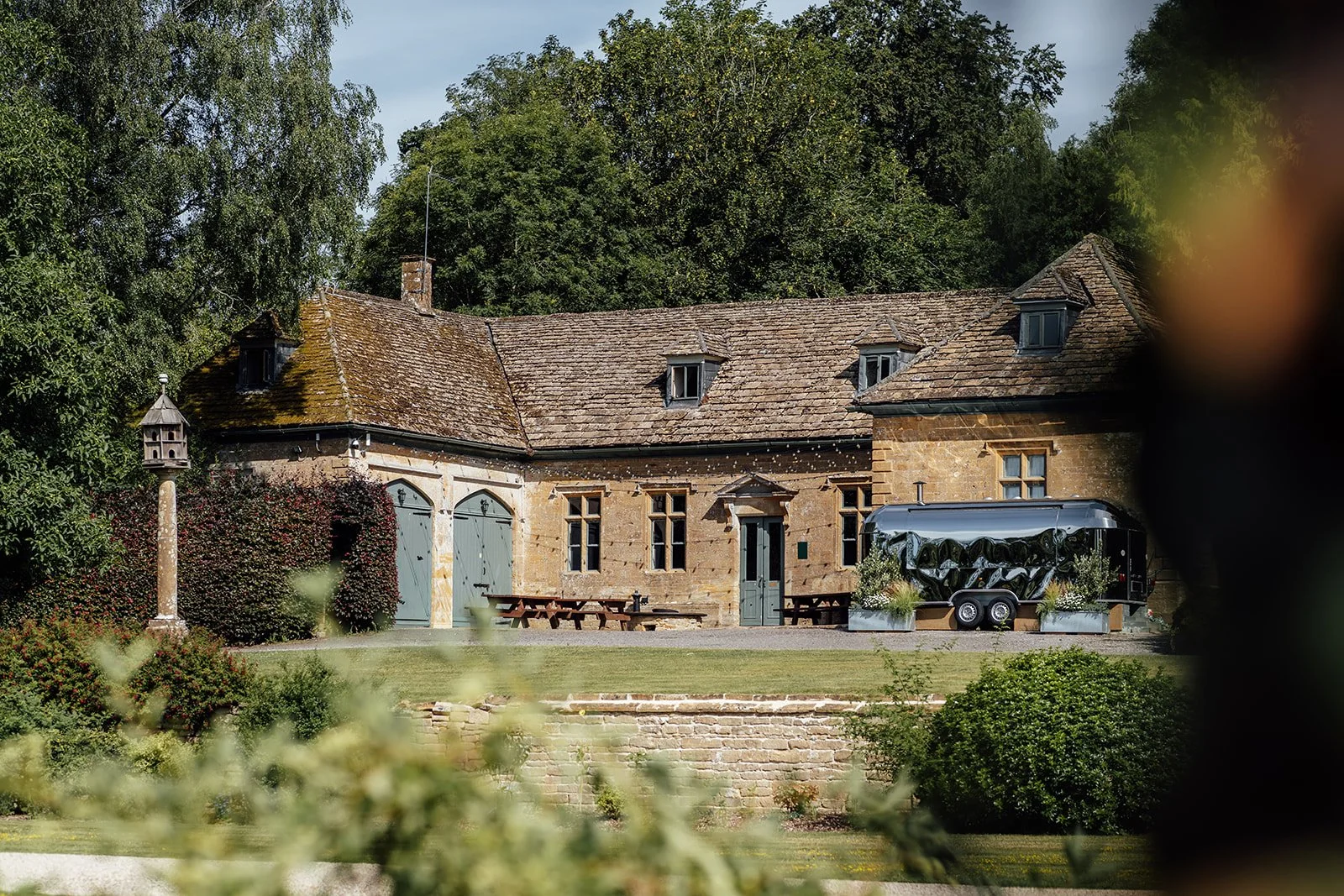 Exterior of The Party Barn at Brympton House in Somerset, with historic stone walls, garden lawn, seating and a silver catering trailer, photographed by Just James Weddings.