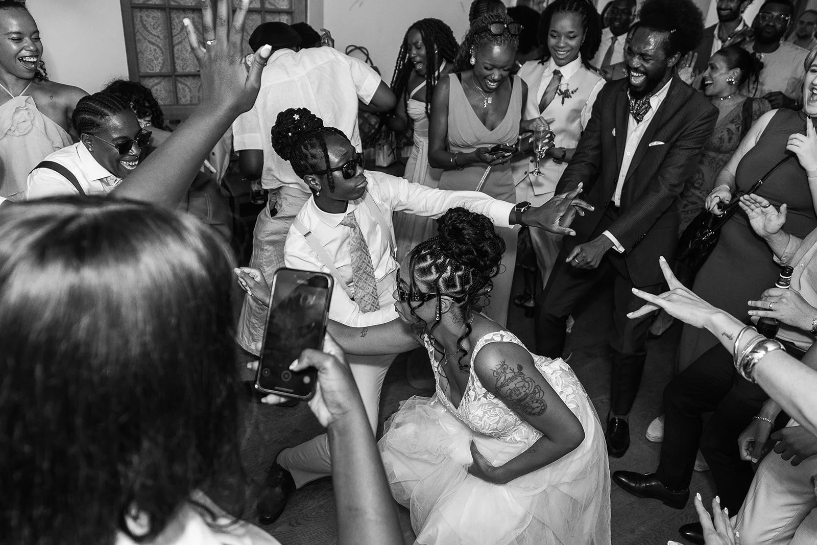 Black and white photo of Kasey and Larisha dancing together in the middle of a lively crowd during their wedding reception at Oaks Farm Weddings in Surrey.