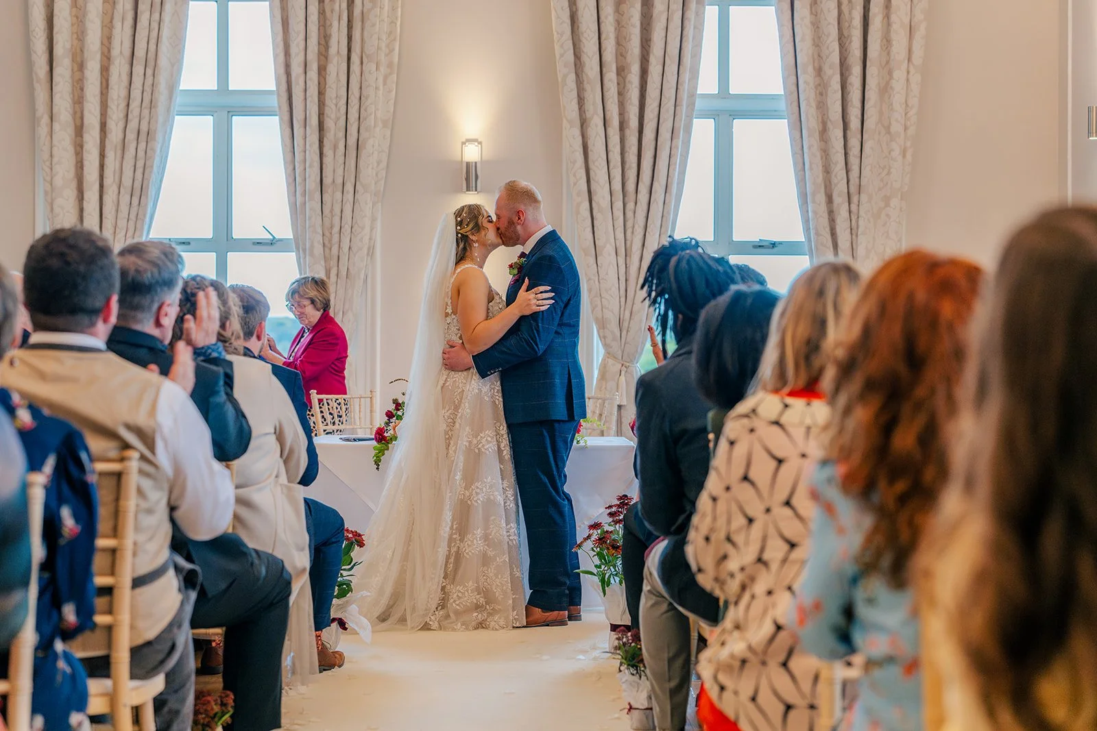 Lucy & Jay sharing their first kiss during their indoor ceremony at Eastwood Park in Gloucestershire, with guests watching, photographed by Just James Weddings for natural ceremony moments.