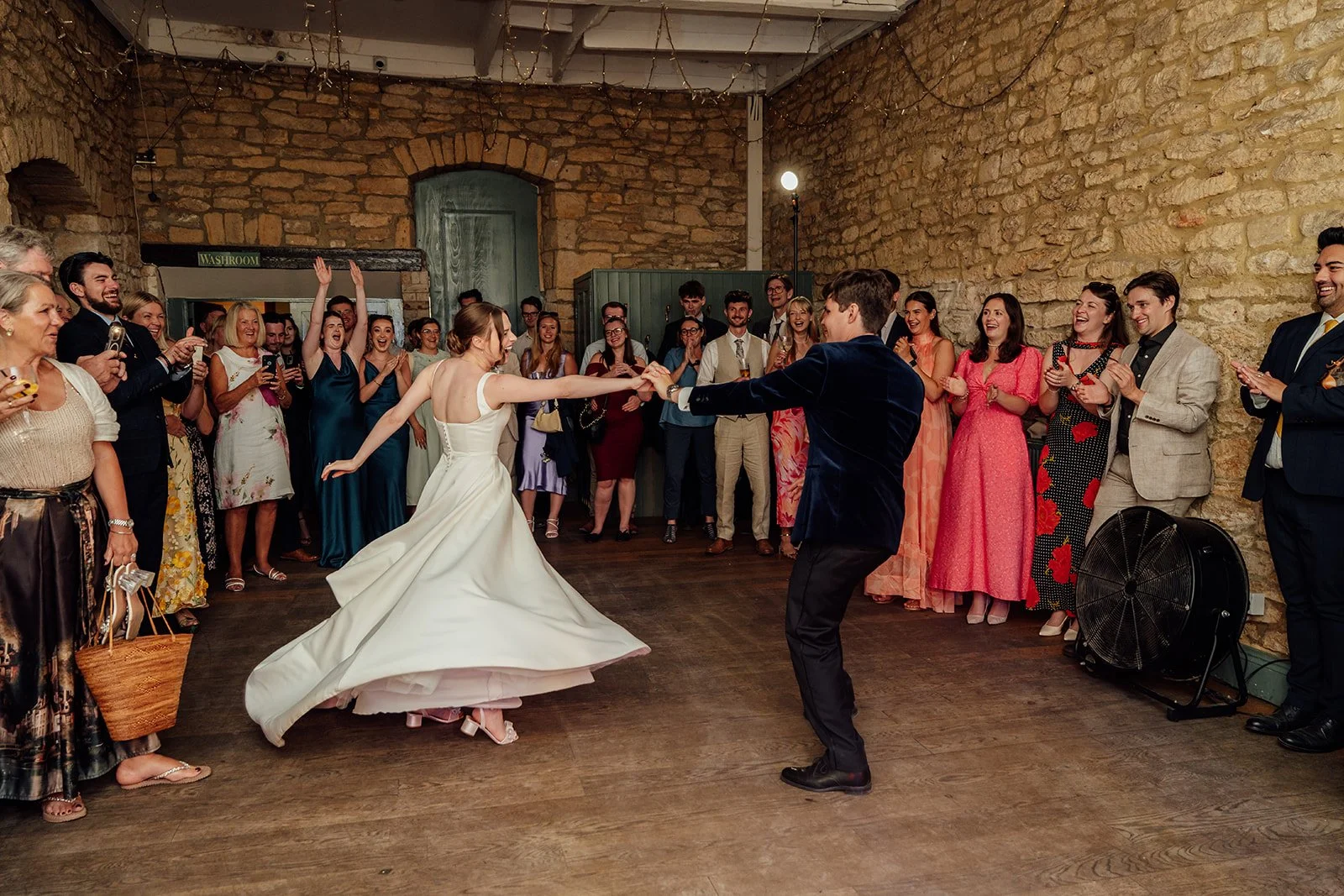 Rachel & Tom spin across the dance floor while wedding guests cheer around them inside Brympton House in Somerset, photographed by Just James Weddings.