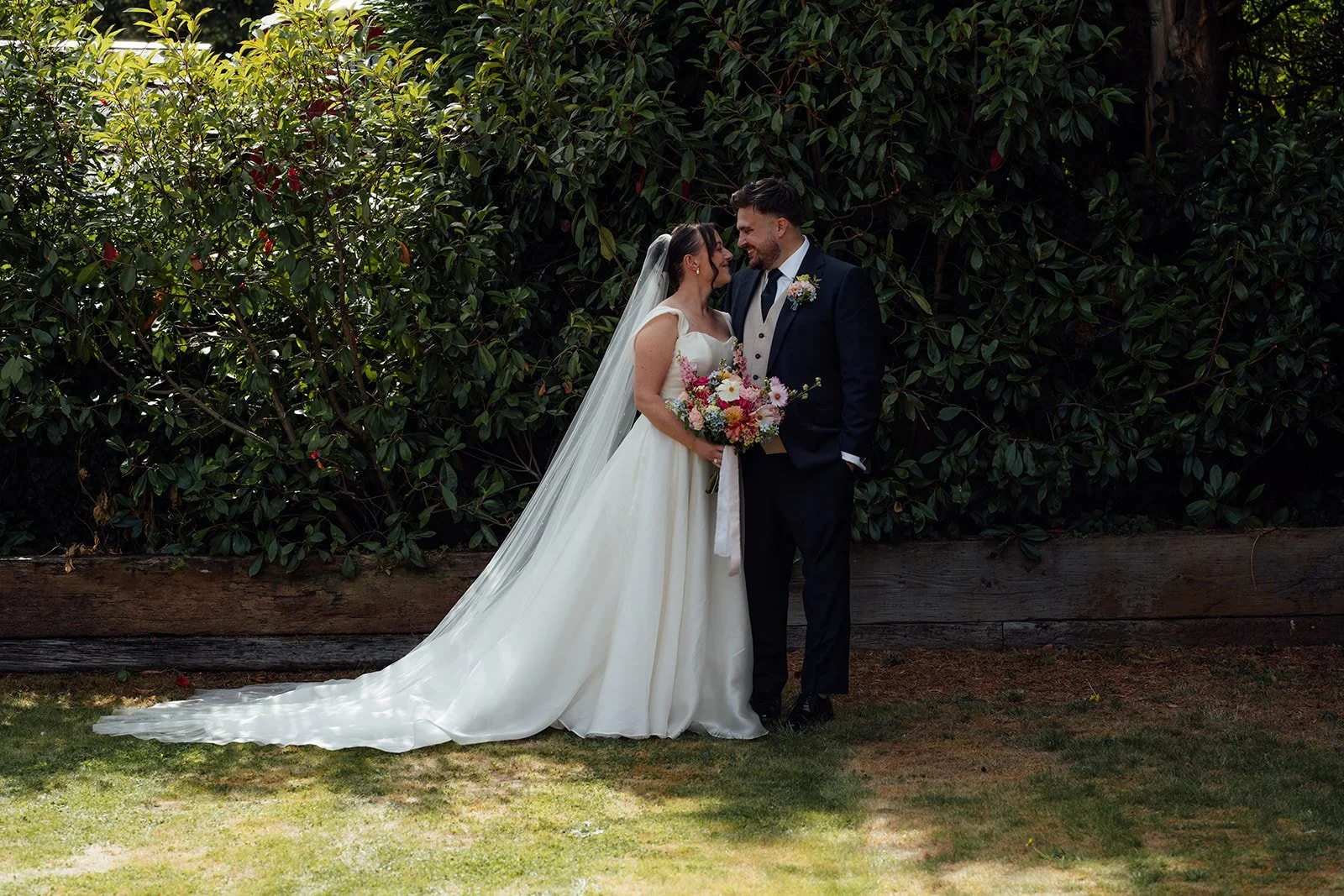 Harriet & Simon smile at each other during relaxed couple portraits in the gardens at Dovecote Events in Oxfordshire, photographed by Just James Weddings.