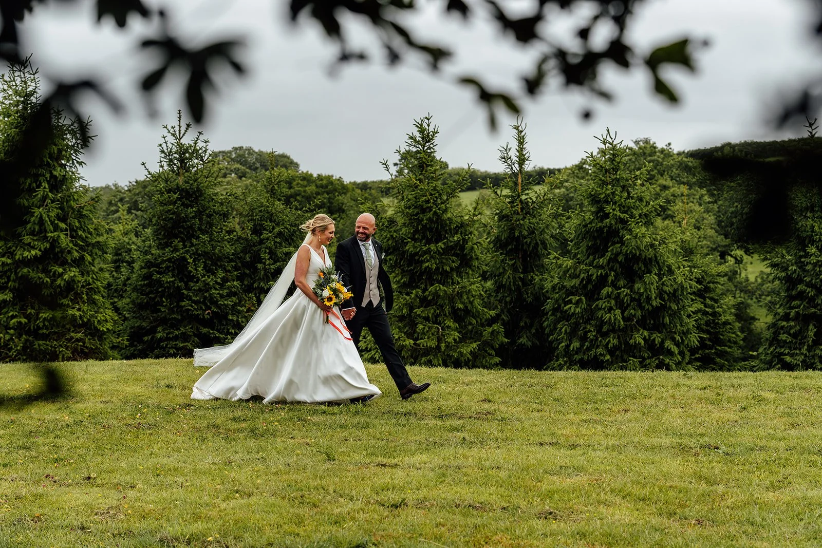 Hannah and Ben walking hand in hand across the grounds during their relaxed countryside wedding at Grays Barn in Devon, photographed by Just James Weddings.