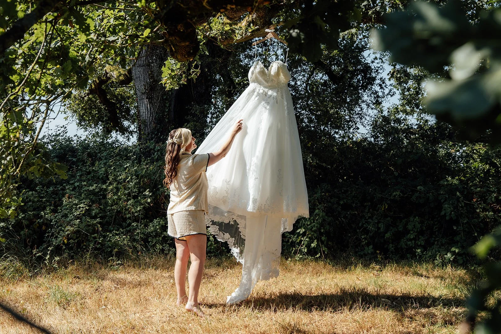 Lucy’s wedding dress hanging from a tree outdoors before her ceremony at Curated Canvas at Noah’s Pond in Somerset, photographed by Just James Weddings.