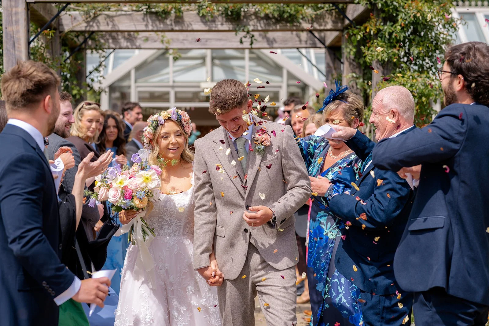 Jaye & Josh walking through colourful confetti after their ceremony at Syrencot in Wiltshire, surrounded by cheering guests, photographed by Just James Weddings.