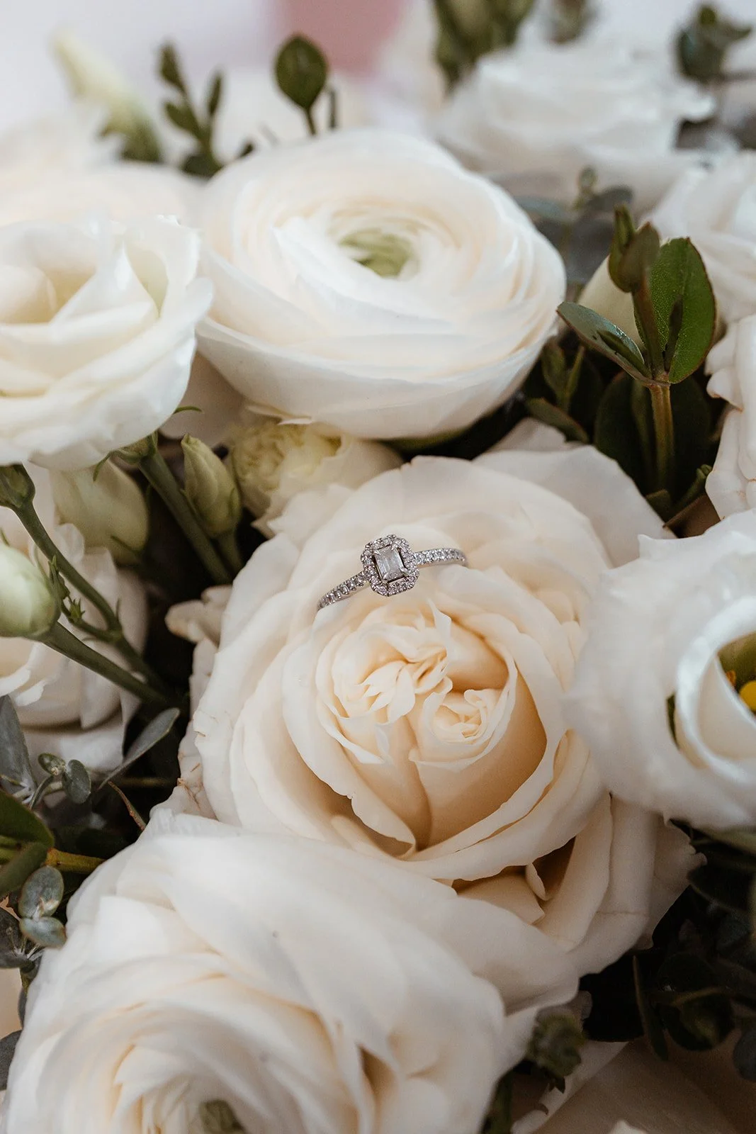 Close-up of Jessie & Jay’s engagement ring resting on soft ivory roses and greenery, photographed during their wedding at Upton Barn & Walled Garden in Devon, UK. Elegant floral textures and natural light create a timeless, romantic detail shot.