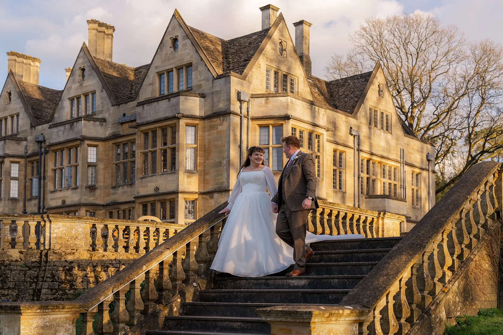 Emily and Josh stand together on the stone steps at Coombe Lodge in Somerset, UK, with the historic country house creating an elegant backdrop for their wedding portrait.