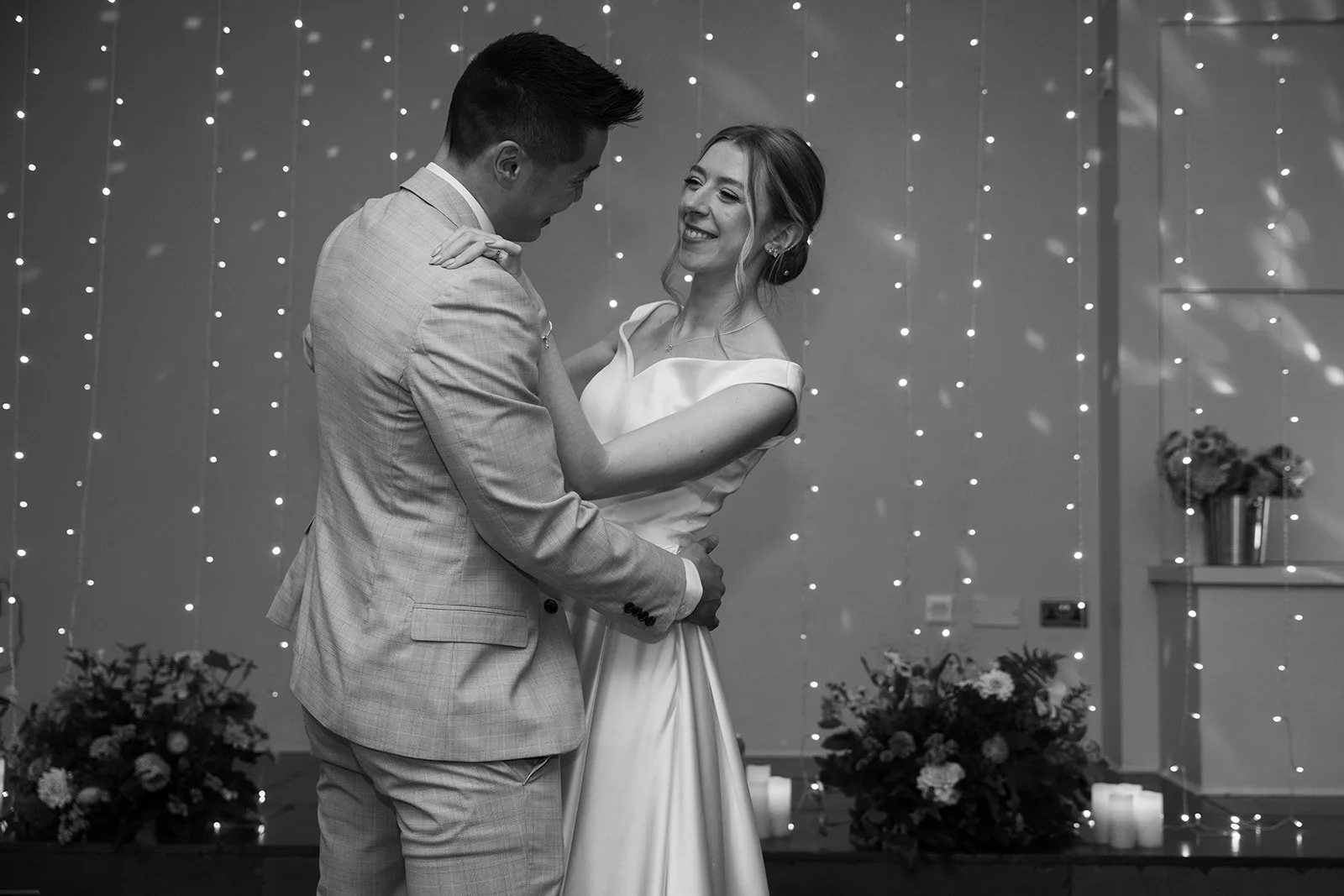Black and white first dance photo of Brian & Josie at Clifton Observatory in Somerset, smiling together beneath fairy lights, photographed by Just James Weddings.