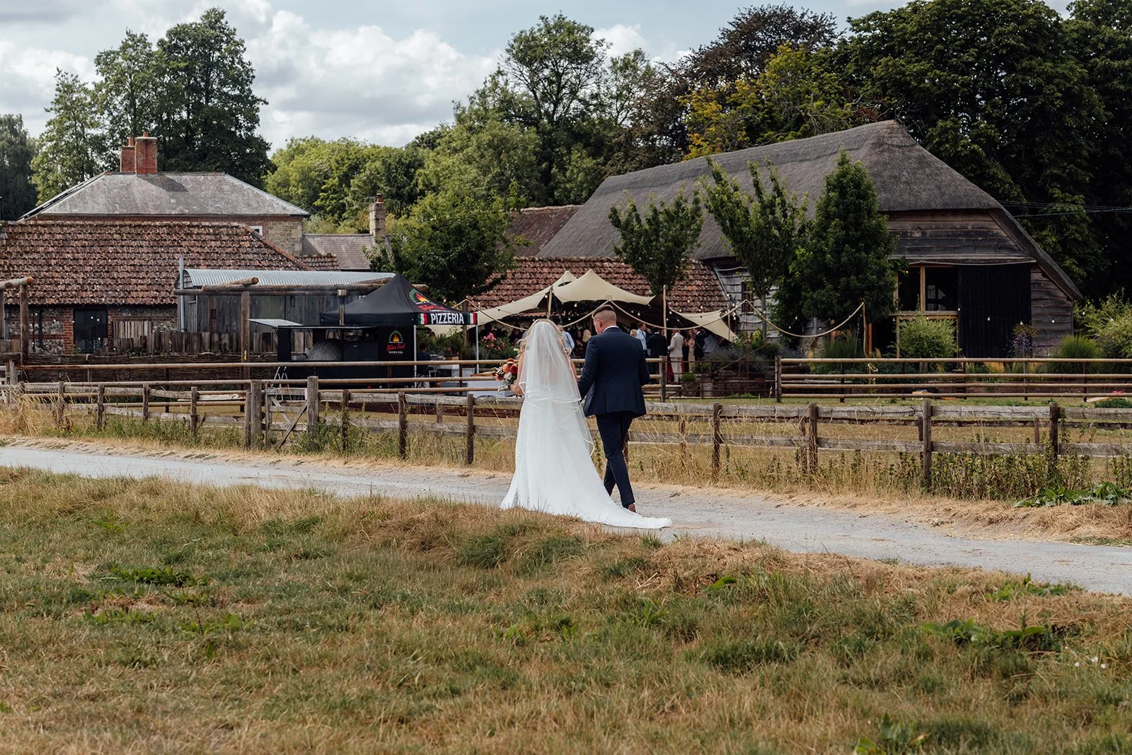 Elise and Tom walking together towards the rustic barns and reception area during their Bowerchalke Barn wedding in Wiltshire, photographed by Just James Weddings.