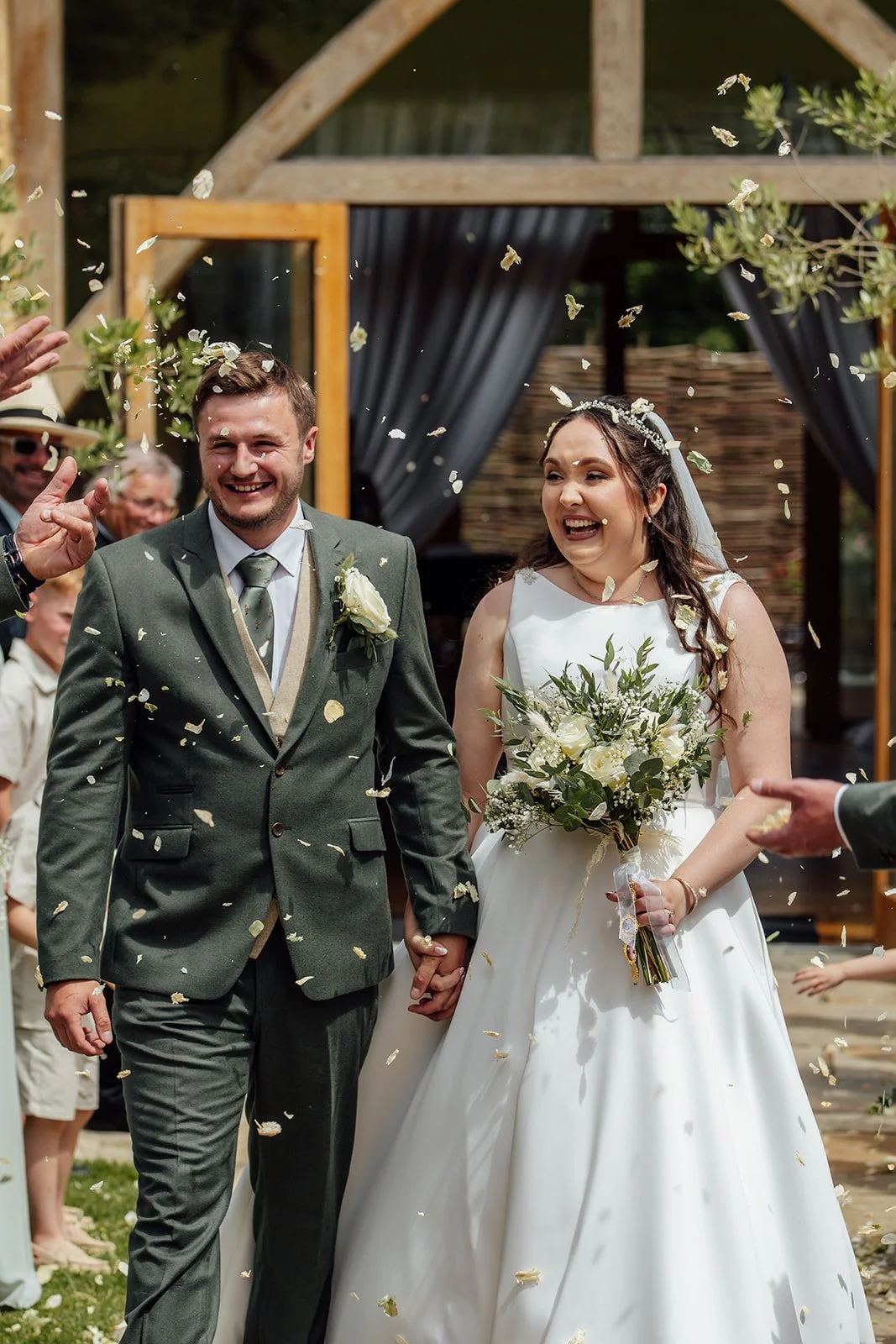 Chloe and Armani smile as guests shower them with confetti outside The Barn at Upcote in Gloucestershire, photographed by Just James Weddings.