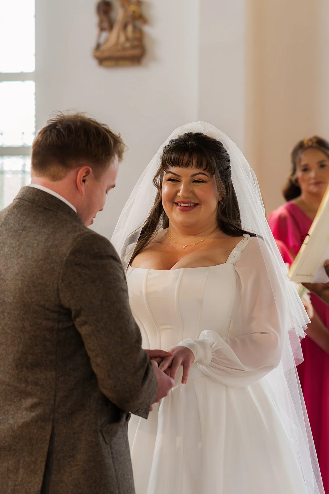 Emily & Josh exchange rings during their wedding ceremony at Coombe Lodge Blagdon, Somerset, UK, as the bride smiles in her veil and gown. A close, emotional moment captured indoors during their Somerset wedding ceremony in soft natural light.