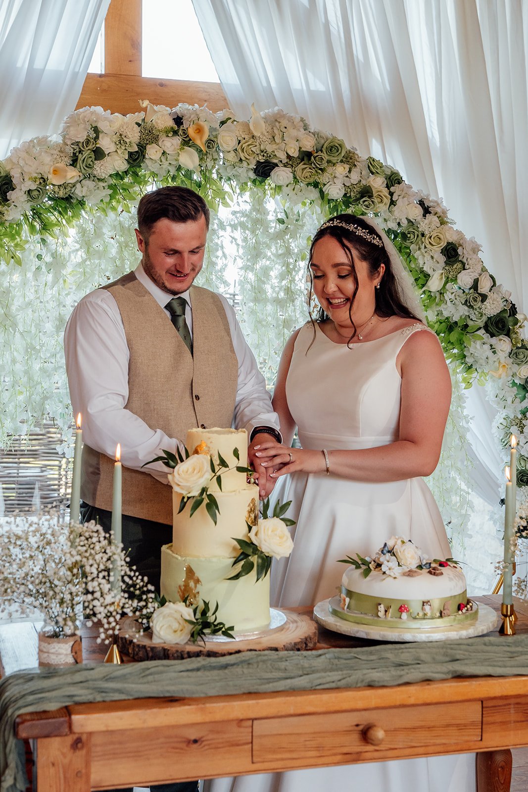 Chloe and Armani smile as they cut their floral wedding cakes during the reception at The Barn at Upcote in Gloucestershire, photographed by Just James Weddings.