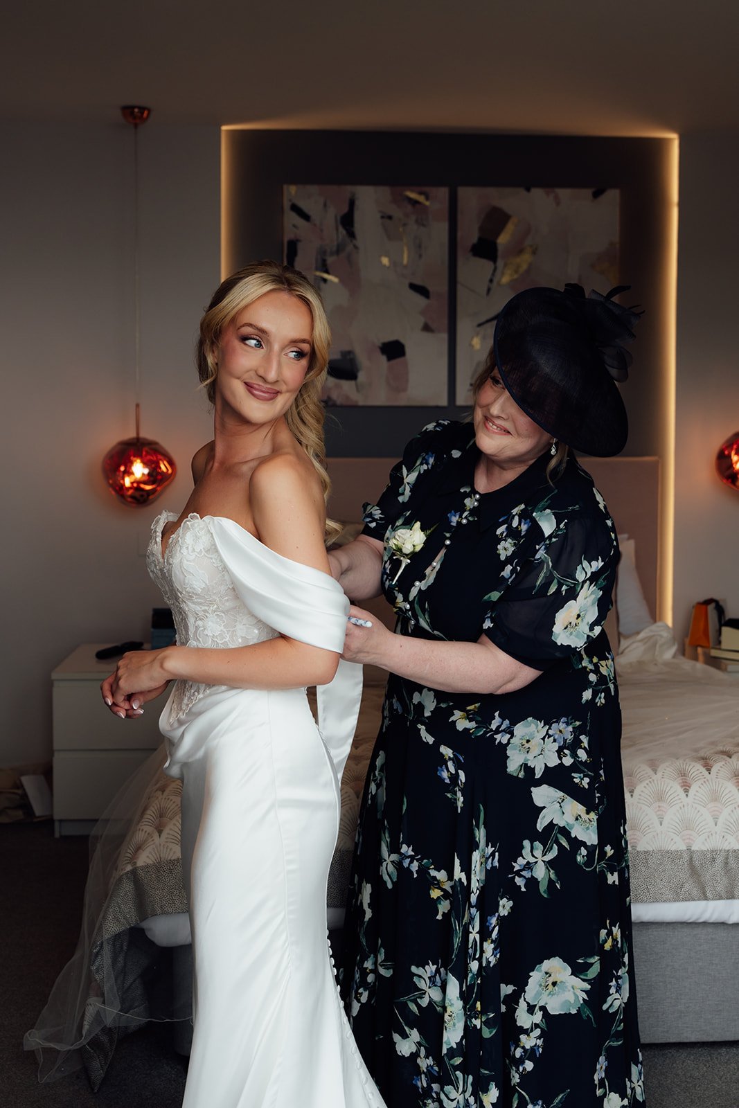 Amy smiles as a family member helps adjust her off-the-shoulder wedding dress during bridal preparations at Sandy Cove Hotel in North Devon, UK.