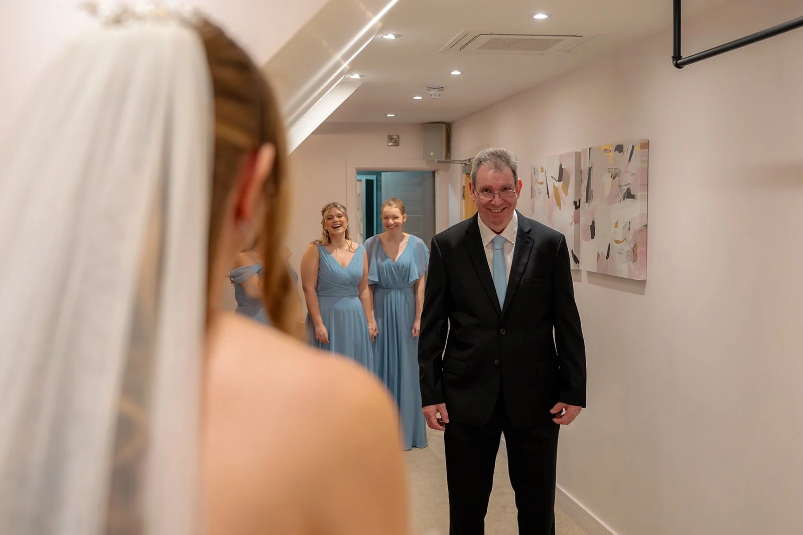 Emotional moment as Hannah’s father sees his daughter in her wedding dress during bridal preparations for Hannah & Cameron’s wedding at Sandy Cove Hotel, North Devon. Bridesmaids smile in the background.
