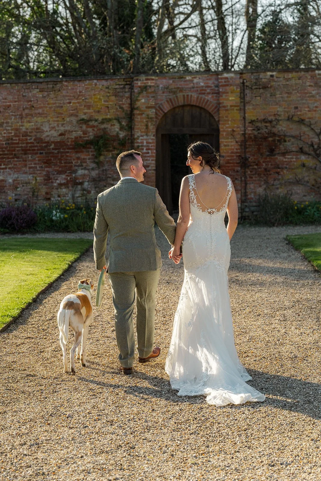 Anna and Chris walk hand in hand with their dog along the gravel path at Elmhay Park in Somerset, UK, glowing in the late afternoon sun. A relaxed, romantic portrait from Anna & Chris’s wedding day, full of warmth, movement, and charm.