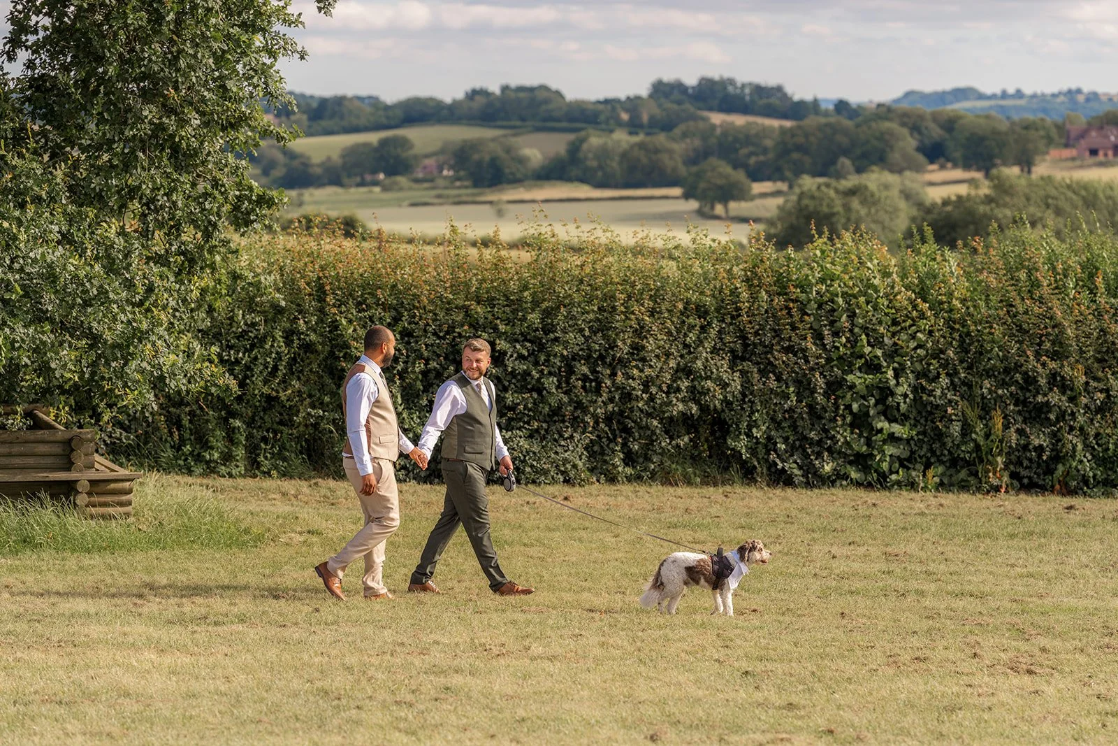 Aaron & Jack walk hand in hand with their dog Milo across the grounds at Rock Village Hall, surrounded by sweeping Worcestershire countryside, photographed by Just James Weddings.