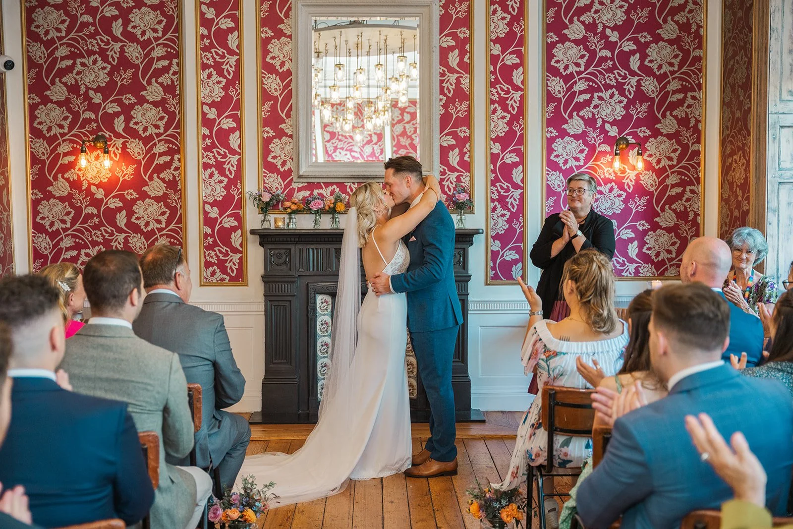 Kristy and Will share their first kiss during their wedding ceremony at No. 4 Clifton Village in Bristol, UK, surrounded by guests in the venue’s elegant ceremony room.