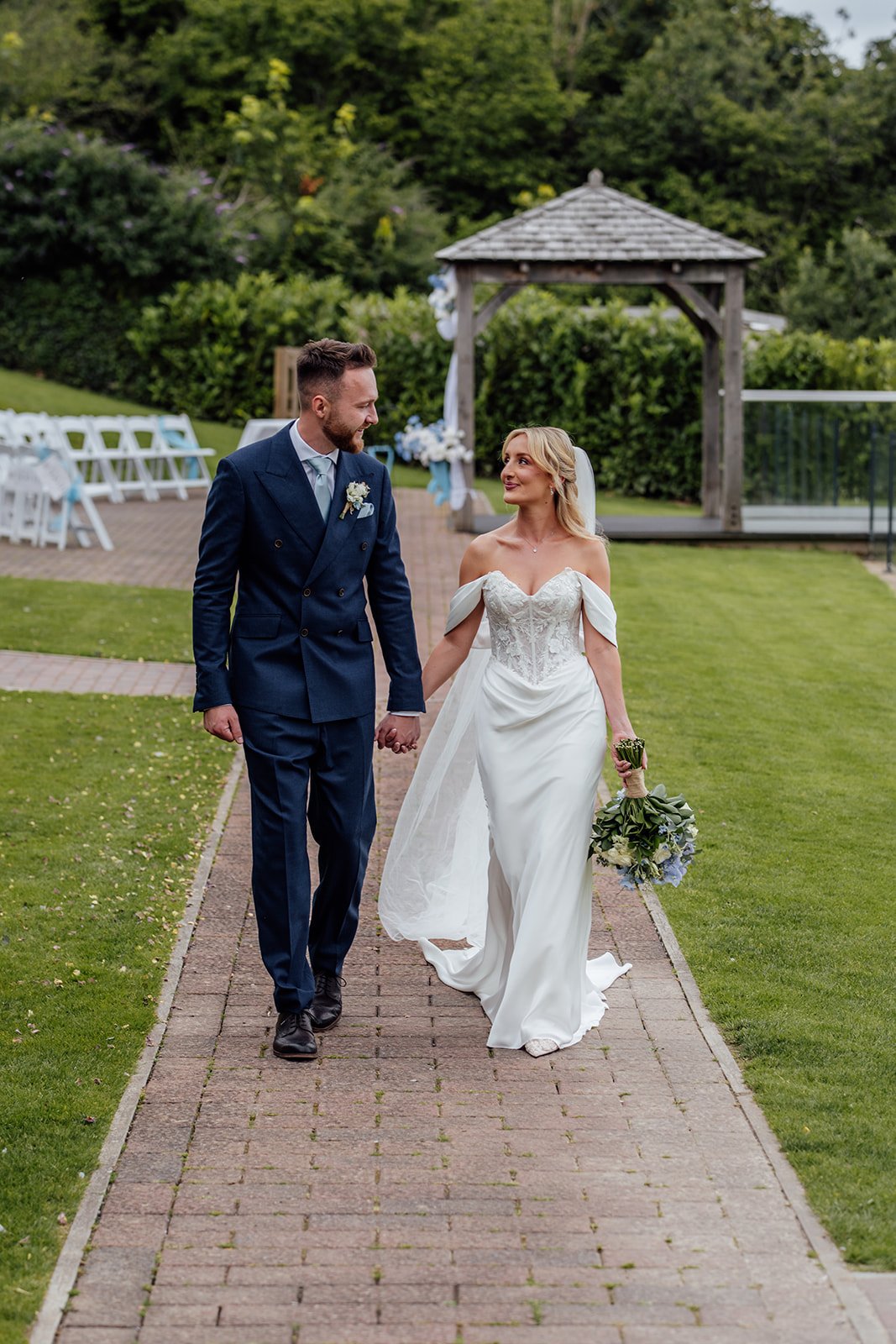 Newlyweds Amy & Connor walk hand in hand through the gardens after their outdoor ceremony at Sandy Cove Hotel in North Devon, UK.