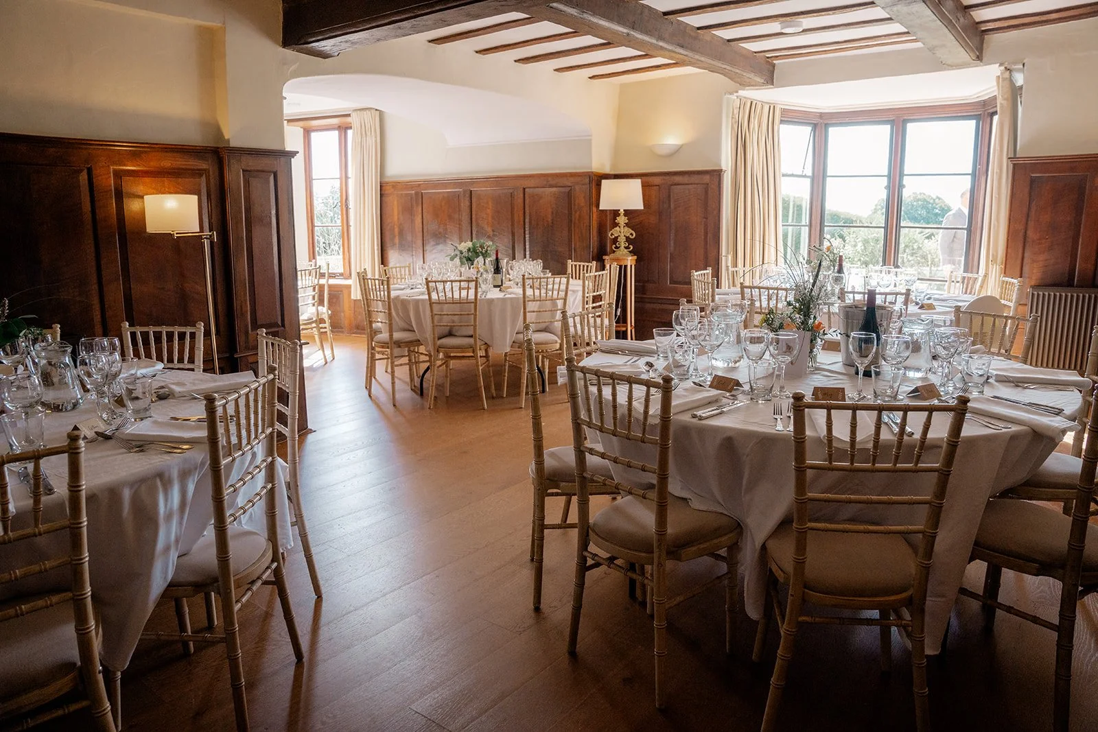 Wedding breakfast room at Broadfield Court in Herefordshire, with round tables, gold chairs, glassware and warm wood panelling, photographed by Just James Weddings for reception inspiration.